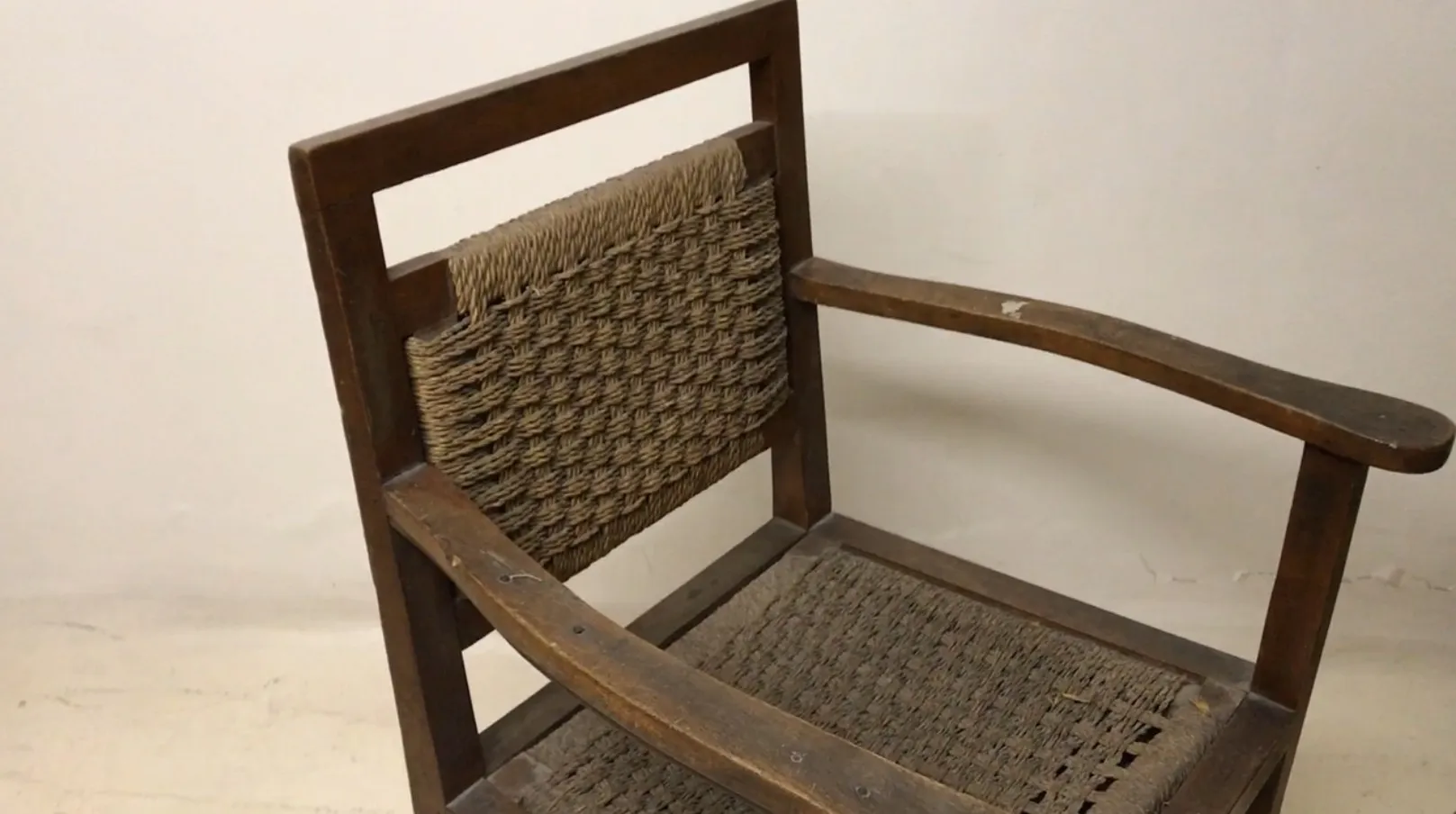 Fauteuil ancien avec dos tissé sur fond clair.
