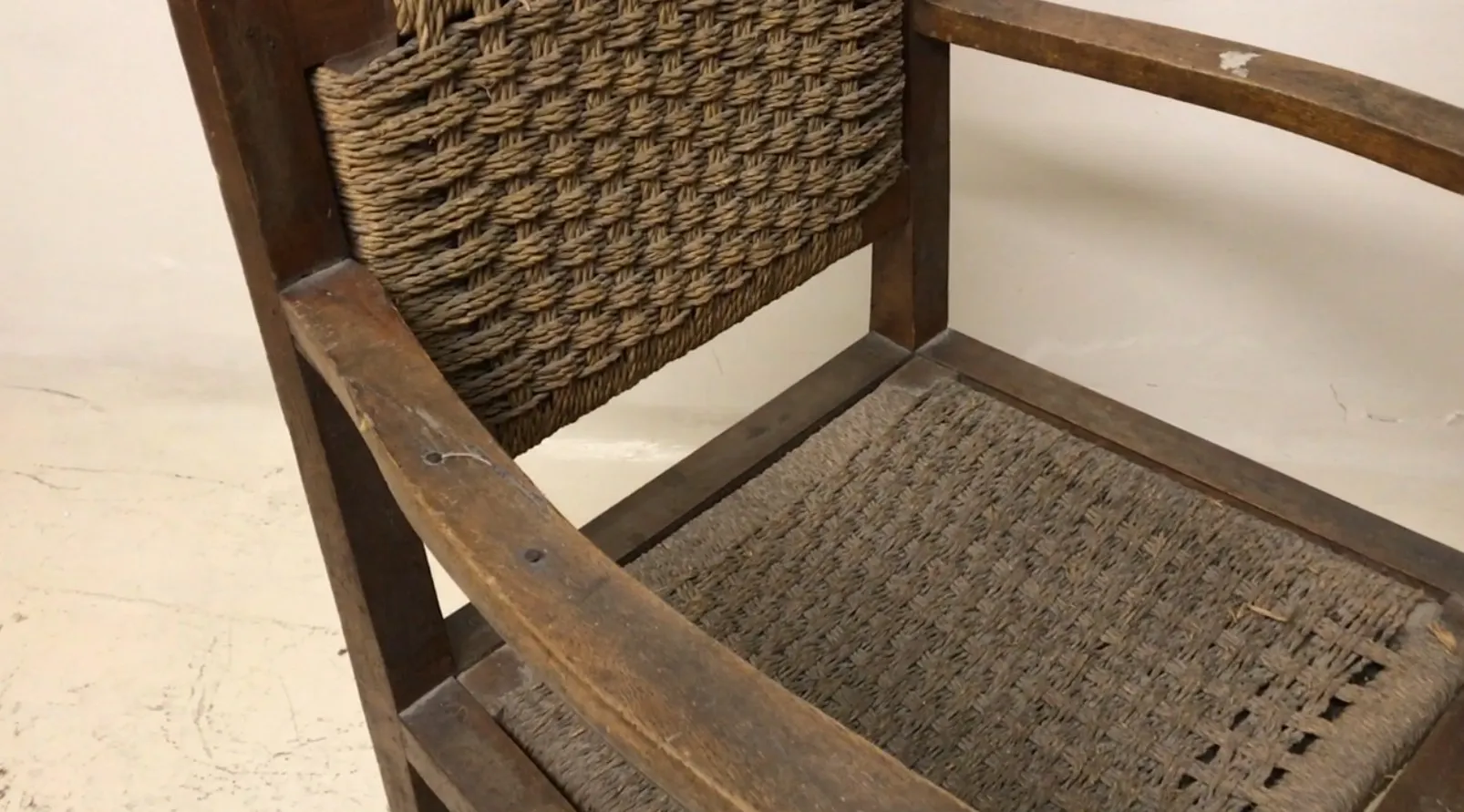 Fauteuil ancien avec dossier tissé dans un cadre neutre.