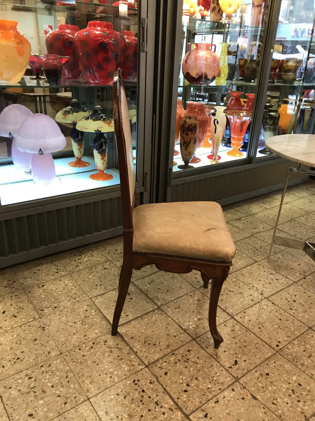 Antique chair with neutral upholstery, background of colorful decorative objects.