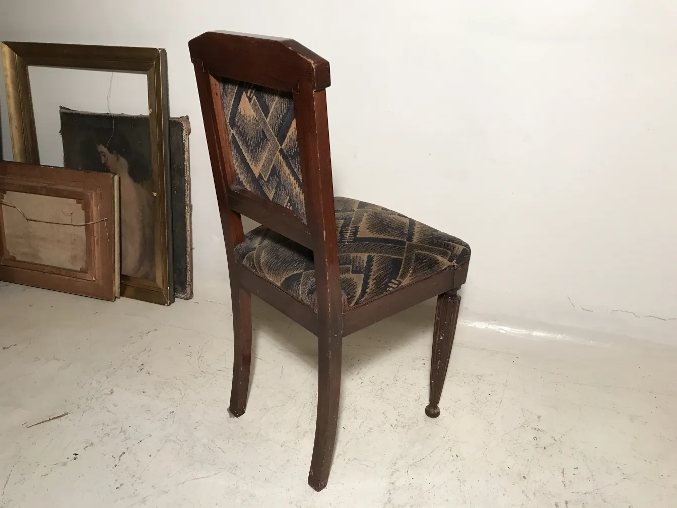 Cadeiras antigas com design clássico prontas para restaurar, cercadas por quadros.