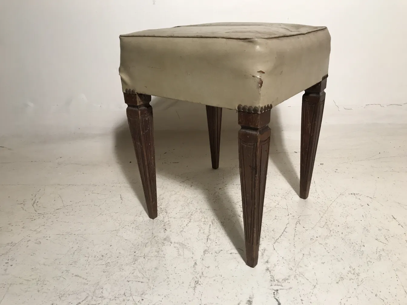 Banqueta antiga com formato quadrado e pernas elevadas que complementa ambientes clássicos.