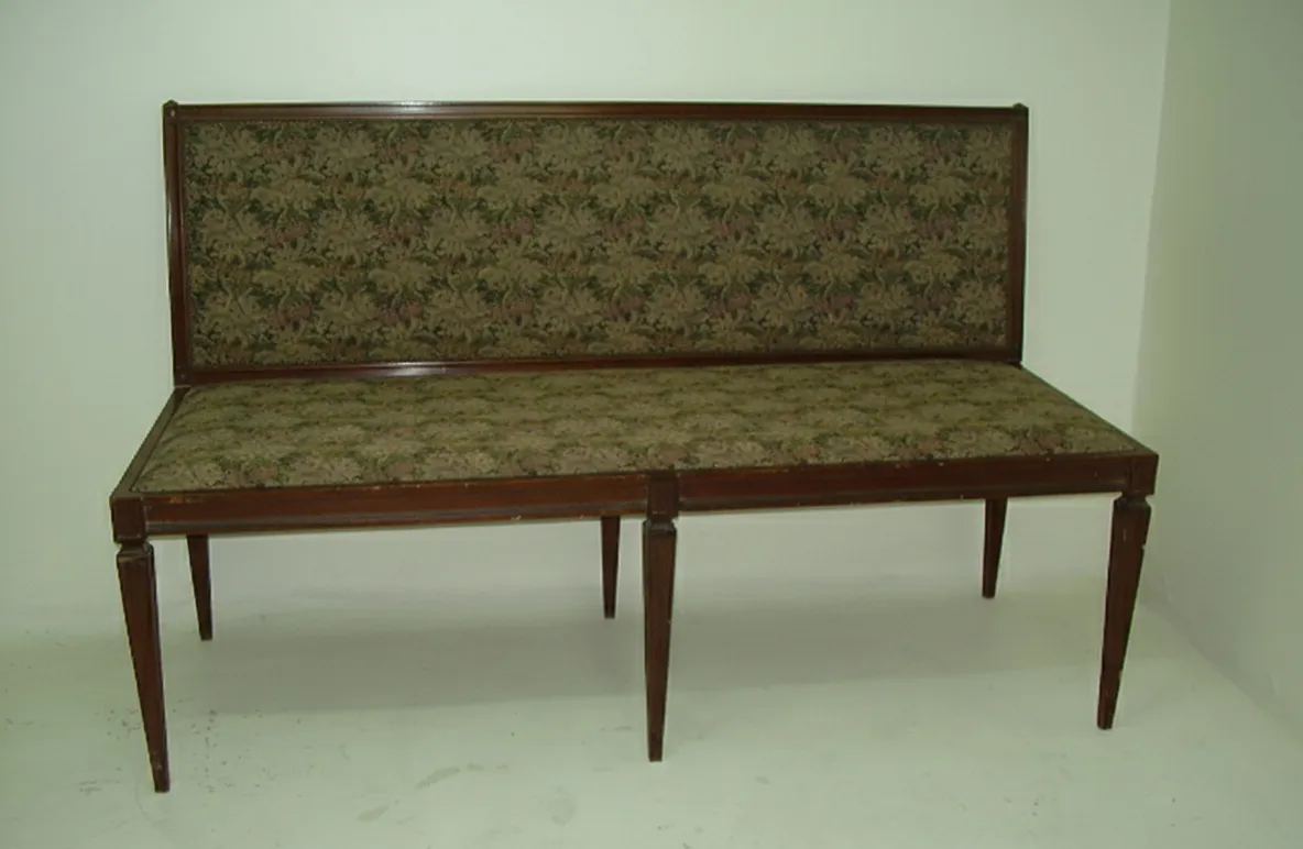 Antiga banqueta com dorso decorativo em ambiente neutro.