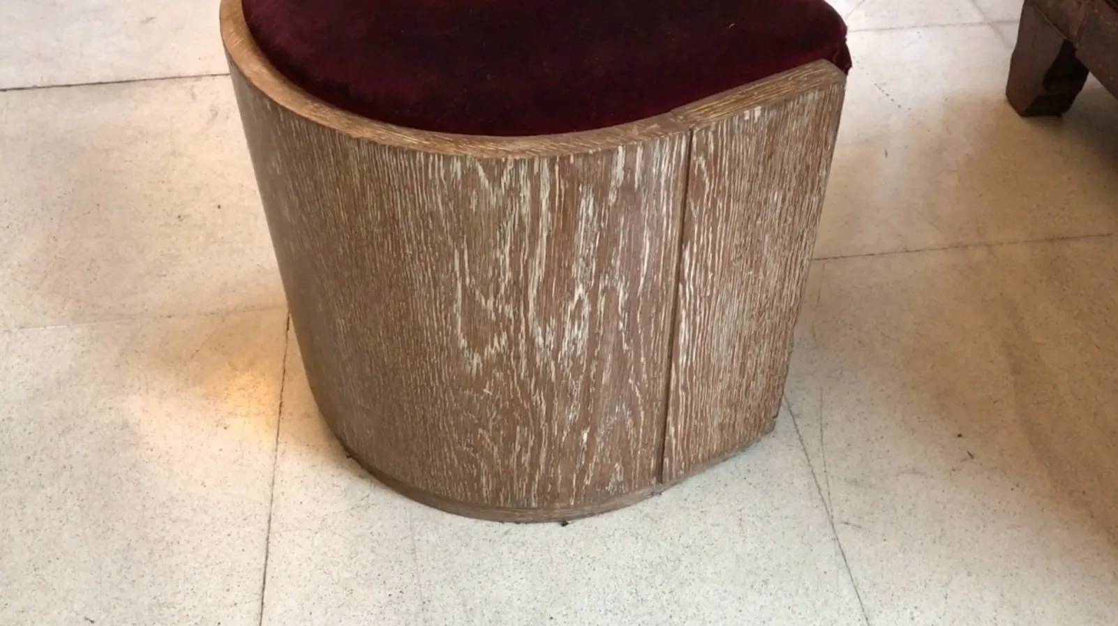 Tabouret antique avec siège en velours bordeaux et forme arrondie dans un cadre neutre.