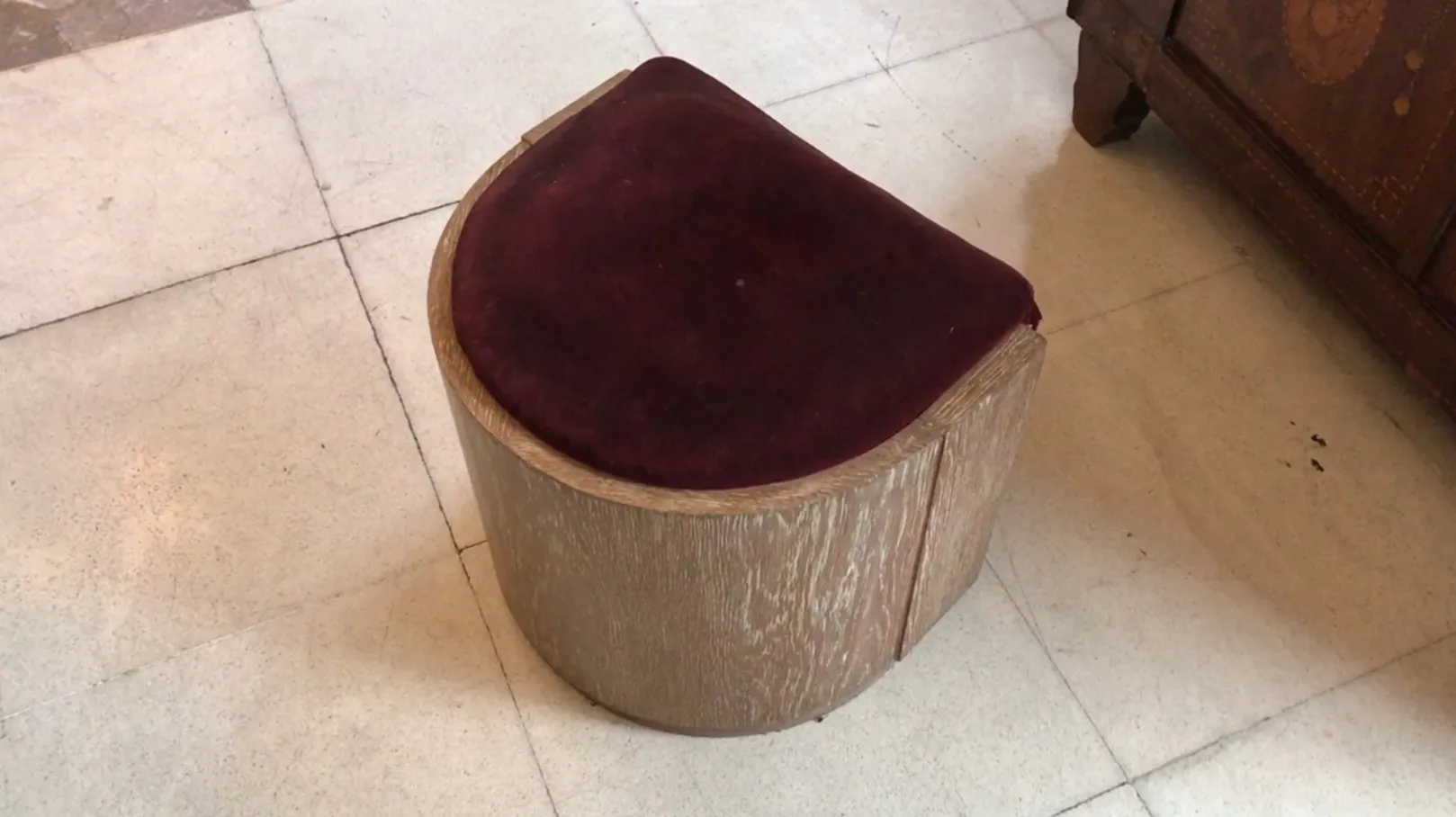 Antique round stool with burgundy upholstery in a neutral setting.
