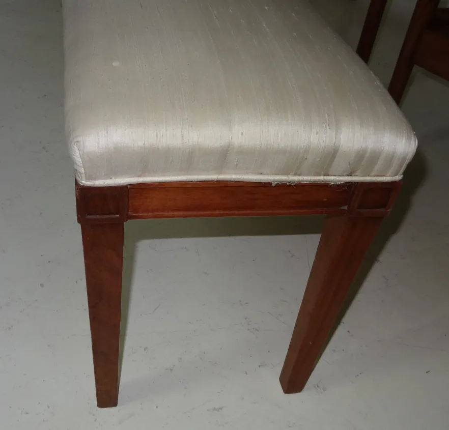 detalhe de uma antiga banqueta com assento claro e pernas retas, ambiente clássico