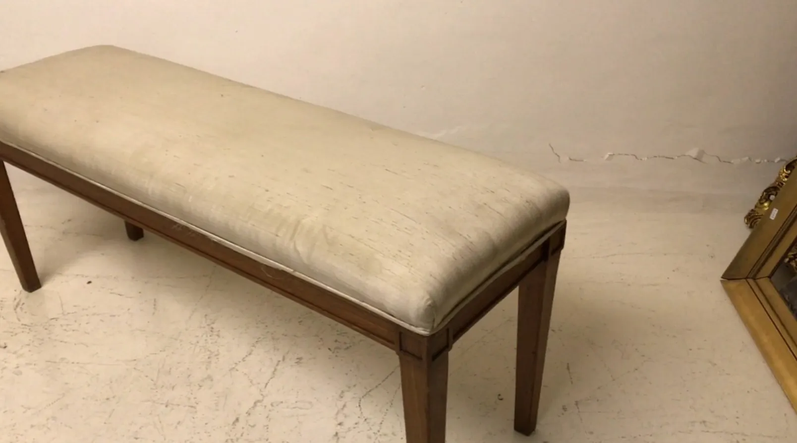 Ancienne banquette avec assise blanche et pieds en bois, simple et élégante, dans un environnement minimaliste.