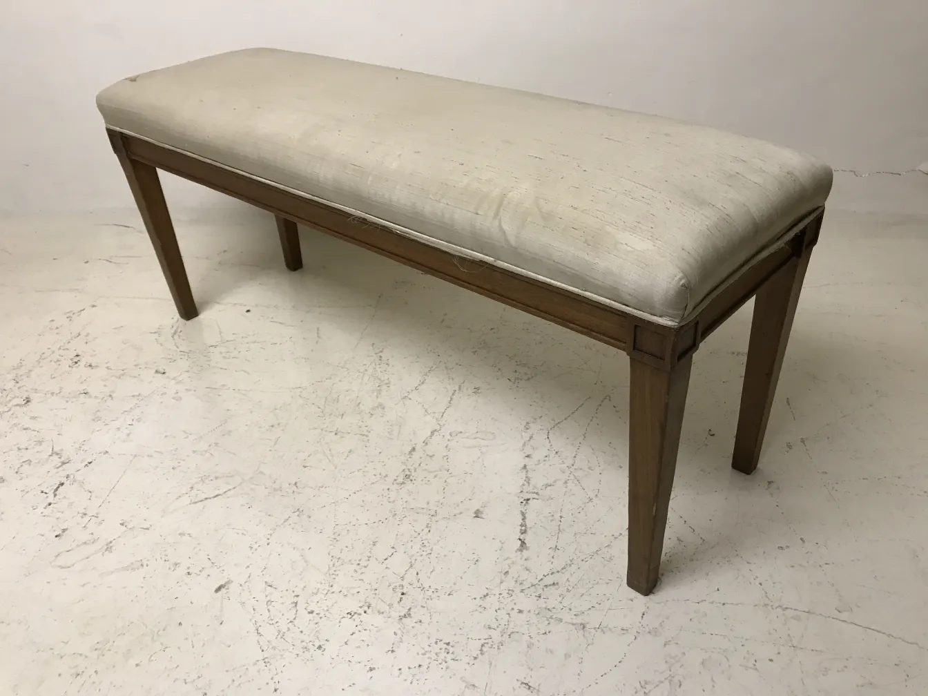 Tabouret ancien avec un coussin clair sur un fond neutre.