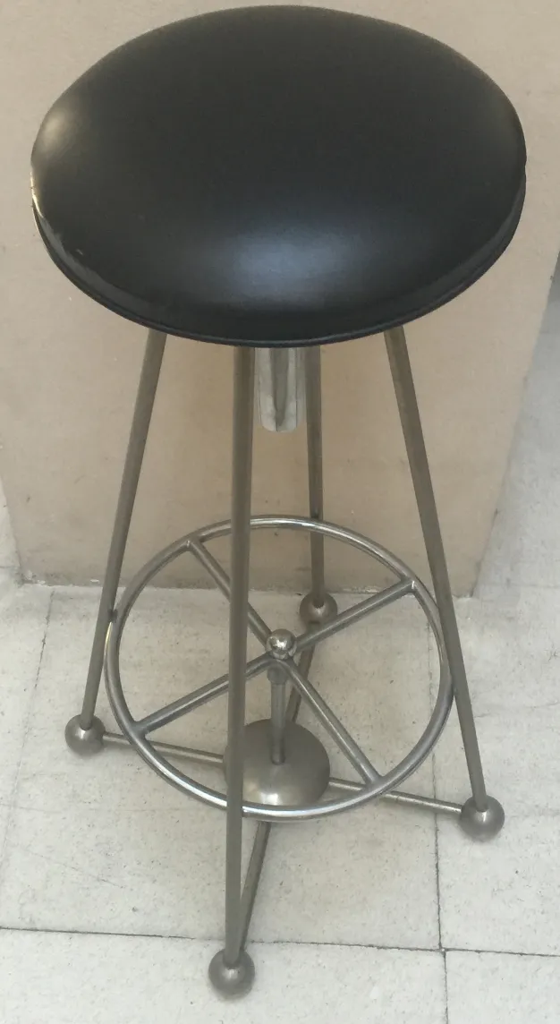 Antiker Hocker mit schwarzer runder Sitzfläche und silberner Basis vor einem schlichten Hintergrund.