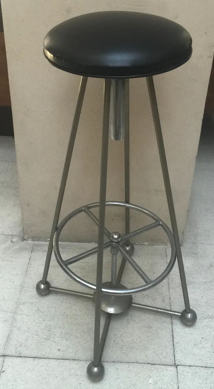 Antiker Hocker mit schwarzem Sitz und Metallbasis in modernem Umfeld.