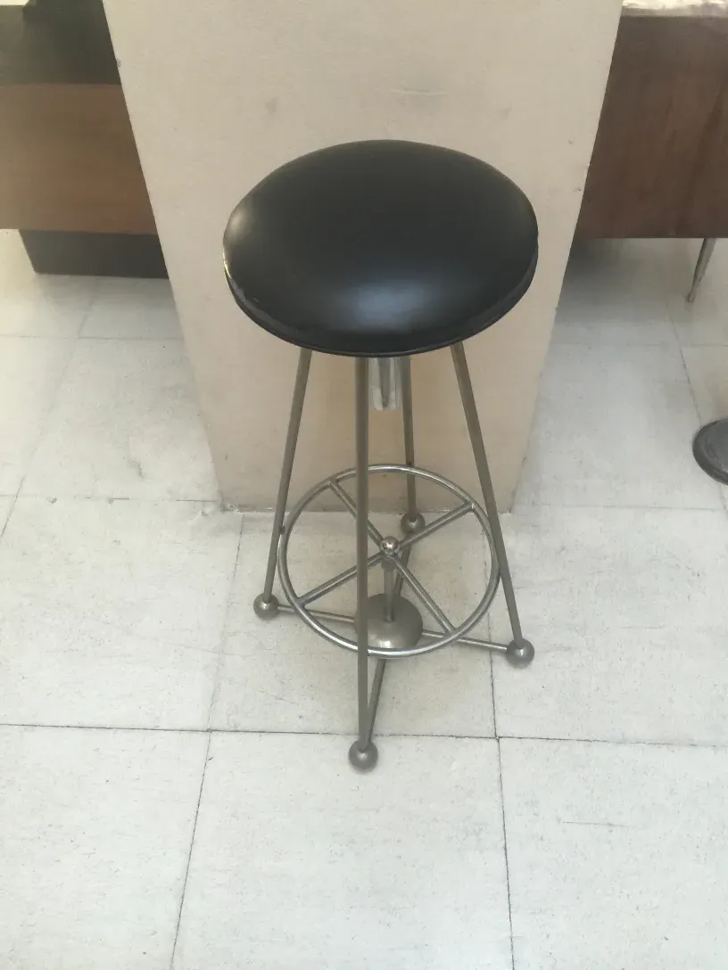 tabouret ancien avec siège noir et base métallique, dans un cadre moderne.