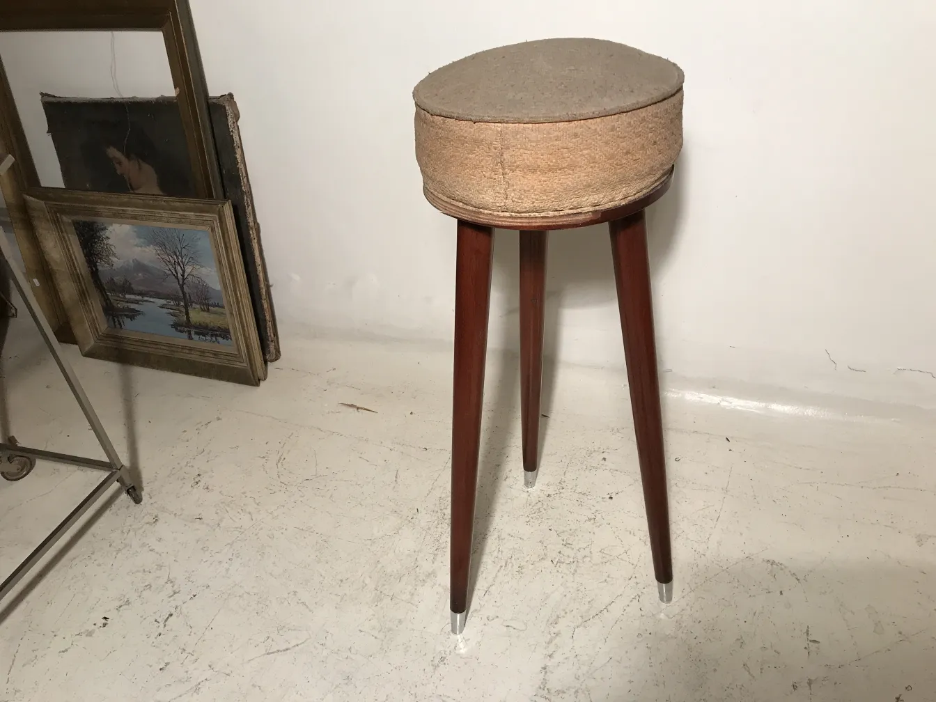 tabouret ancien à trois pieds, assise ronde, arrière-plan avec cadres de tableaux