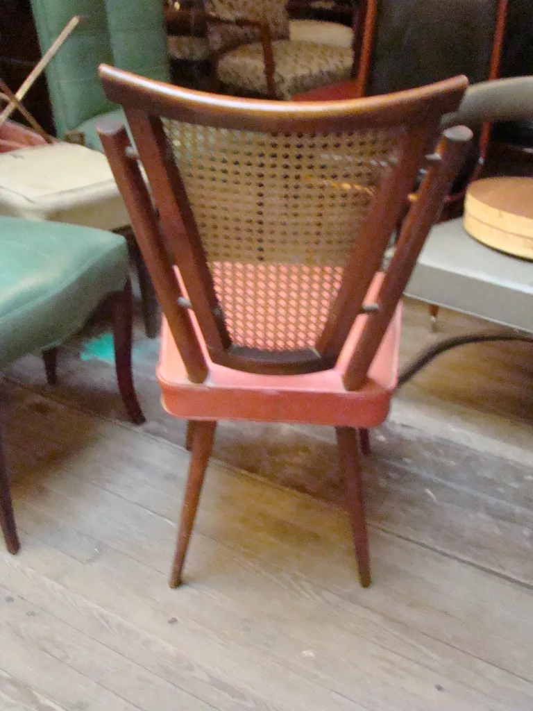 Four antique chairs, one with a woven backrest, in a cozy setting with various chair styles.