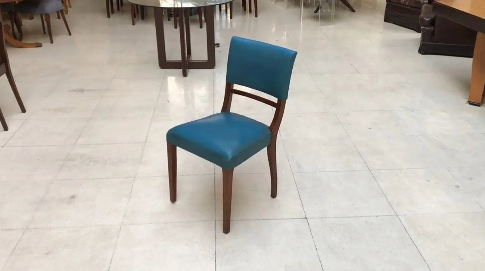 6 antique chairs in various colors placed in a bright setting.