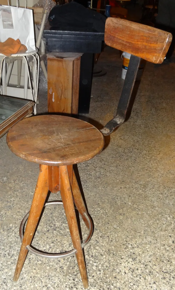 banqueta de madera con patas de trípode y respaldo, en un ambiente antiguo