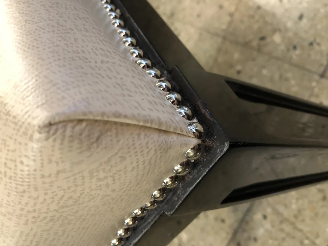 Silver details on the corner of an antique stool with light upholstery.