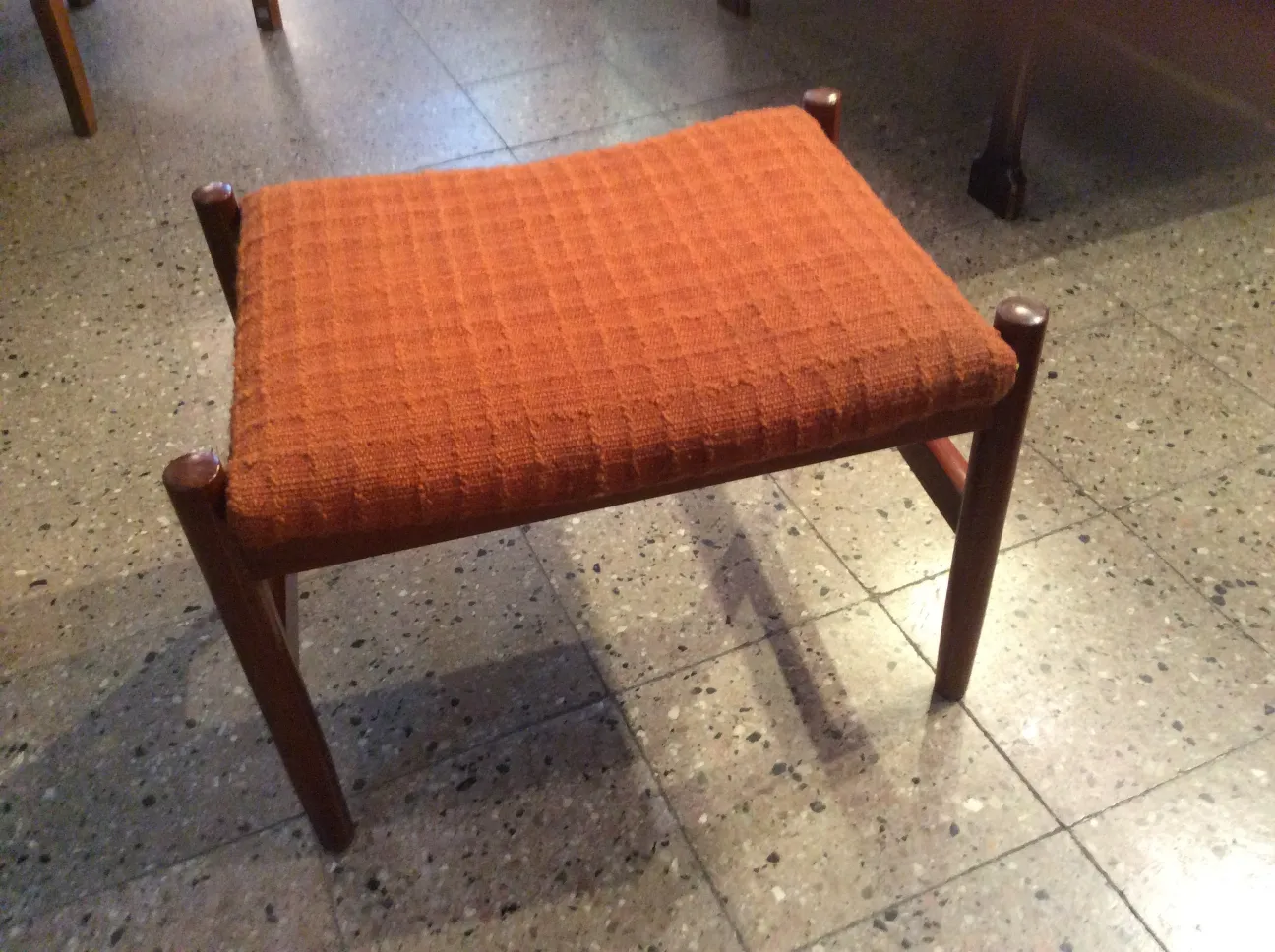 Tabouret ancien avec assise rembourrée orange, dans un cadre rétro.