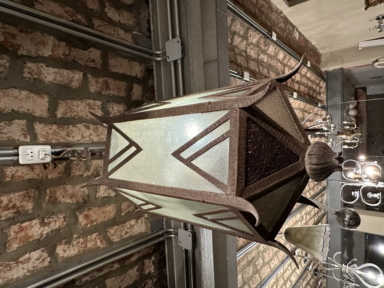 Antique glass lantern with decorative details and a brick background.