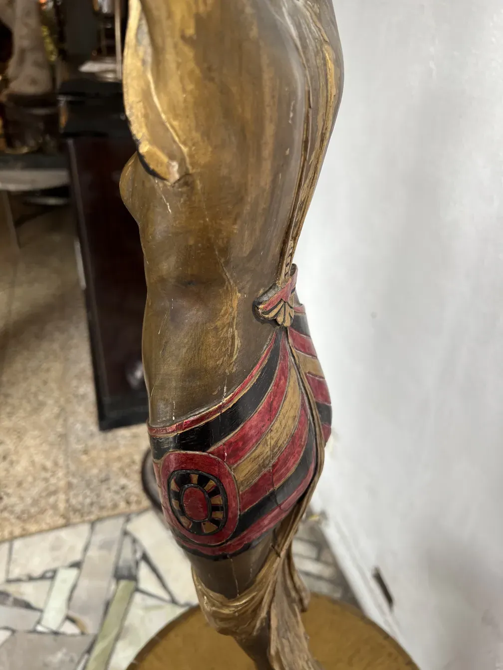 प्राचीन मूर्ति जिसमें लाल और सुनहरे सजावटी तत्व हैं, एक पारंपरिक परिवेश में