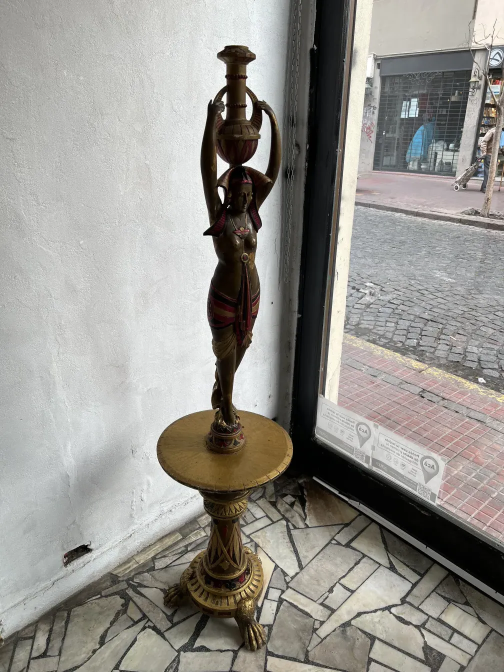 Scultura antica di donna che tiene un bicchiere con dettagli decorativi.