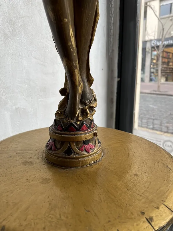 Sculpture ancienne avec base dorée et détails rouges et noirs, mettant en valeur des pieds.
