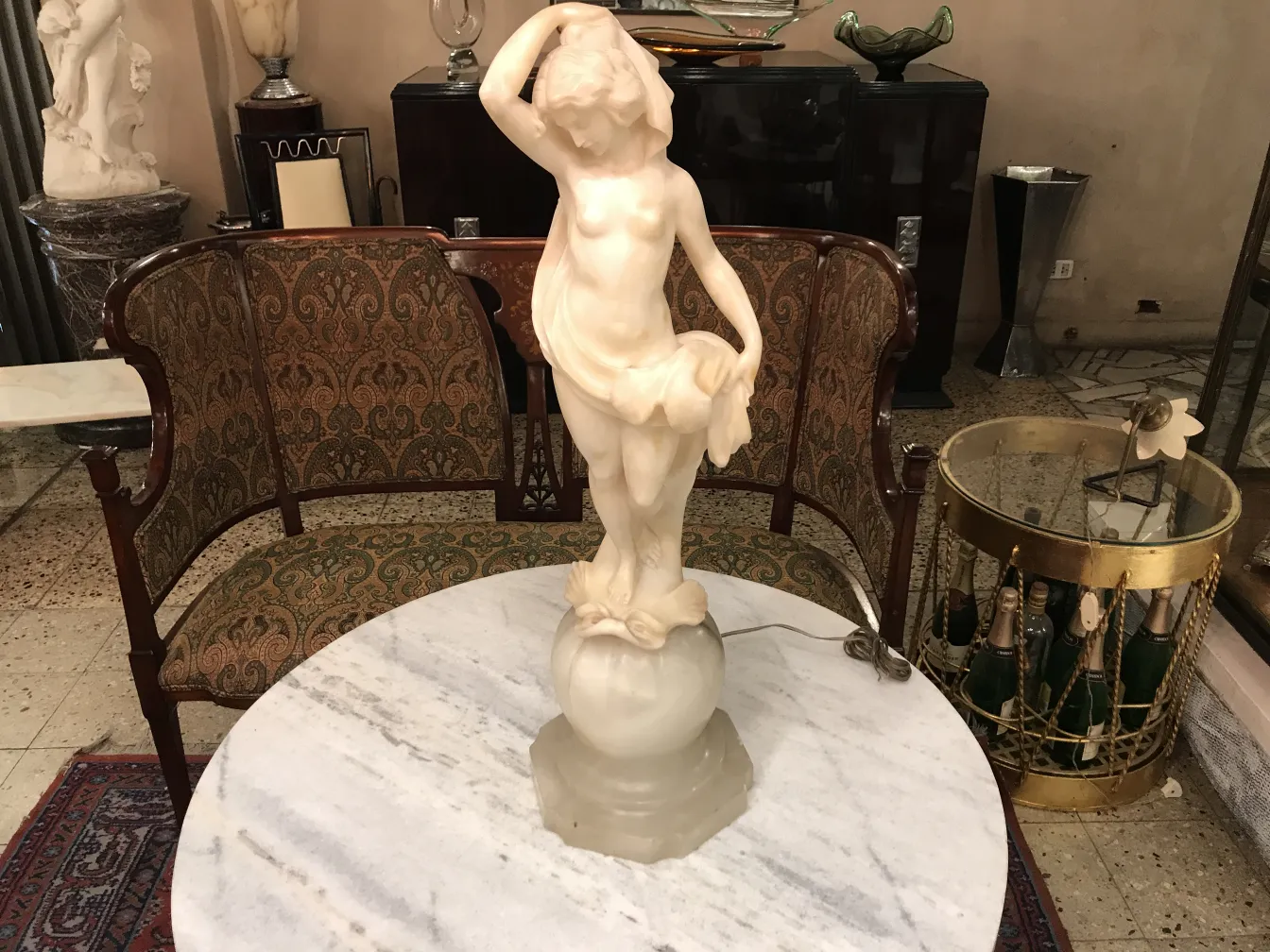 Escultura antigua de figura femenina en mármol, con detalles delicados, situada sobre una mesa de mármol.
