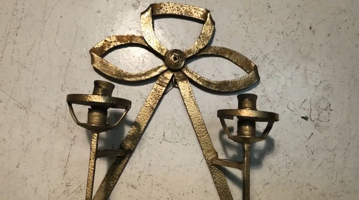 Applique antiche con design a fiocco, che illuminano dolcemente una parete bianca, creando un'atmosfera accogliente.