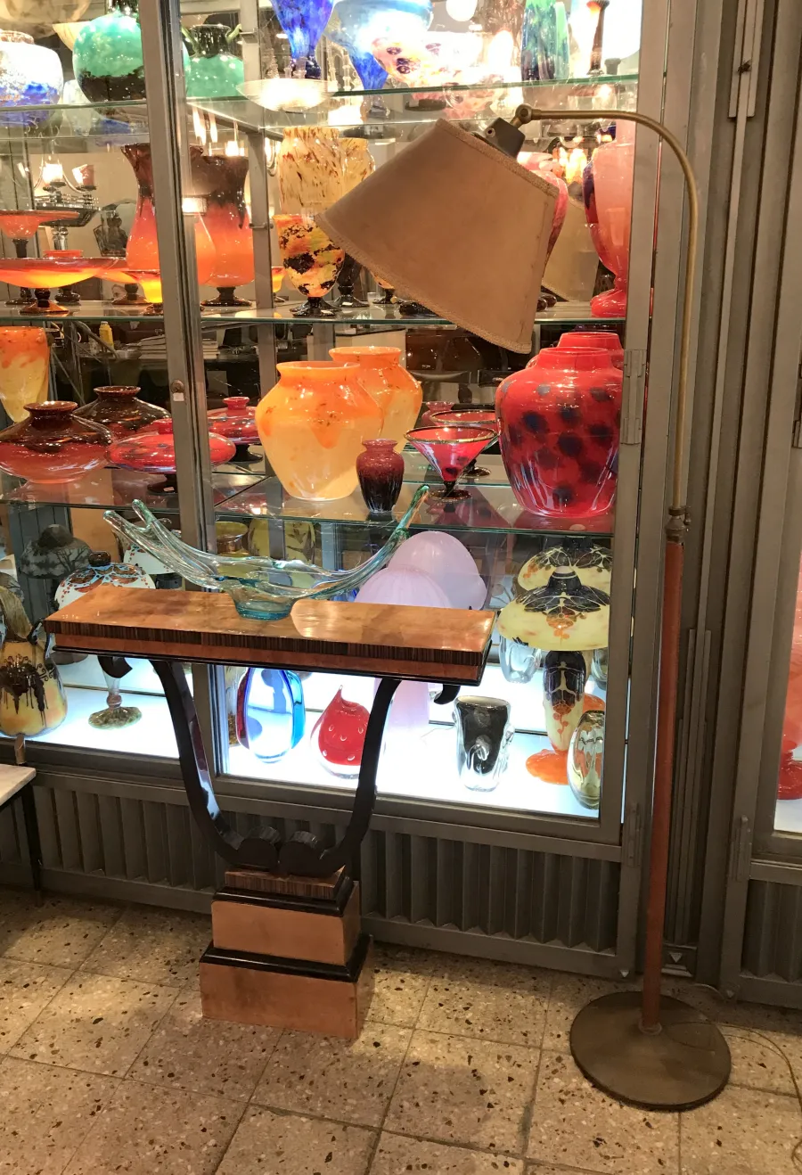 antike stehleuchte mit beigem Schirm und dekorativem Fuß, umgeben von bunten Glasvasen