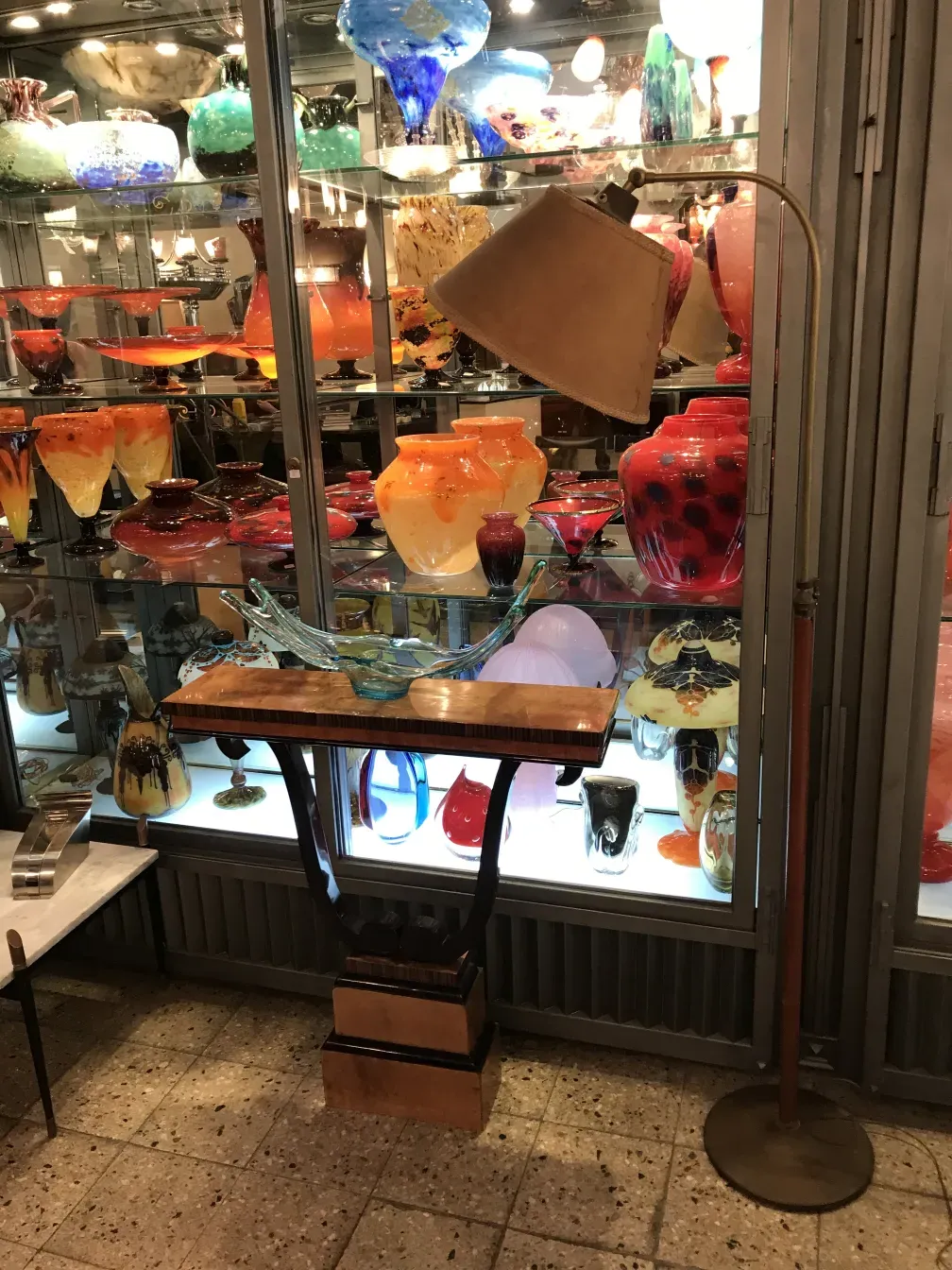 Lámpara de pie antigua Art Deco en exhibición entre elegantes objetos de vidrio.