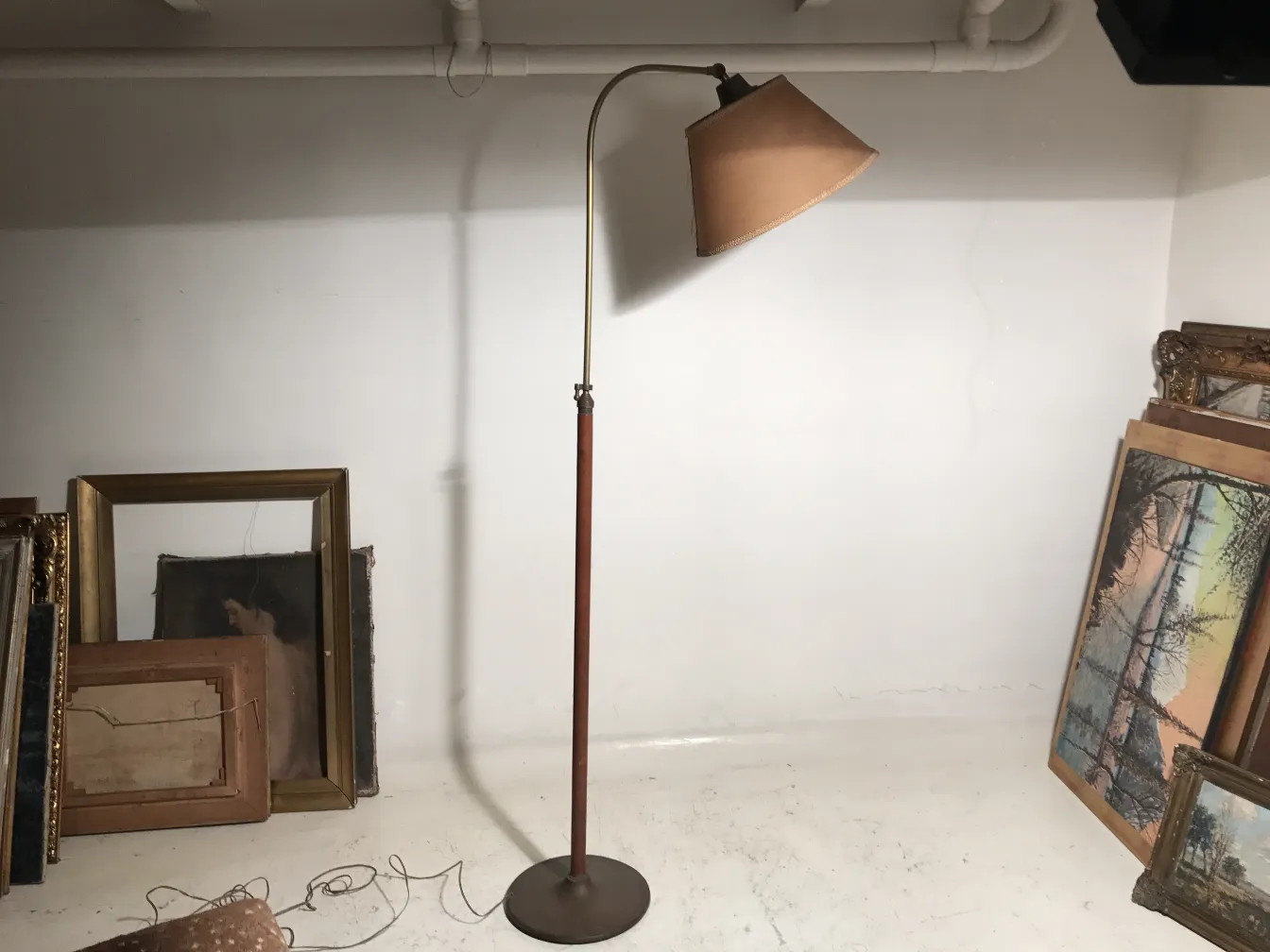 Lámpara de pie antigua con base redonda, sombra marrón y fondo blanco. Decoración en ambiente con cuadros antiguos.