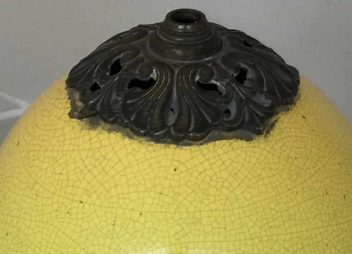 Lámpara de mesa antigua de color amarillo con diseño art deco y detalles decorativos en la parte superior.