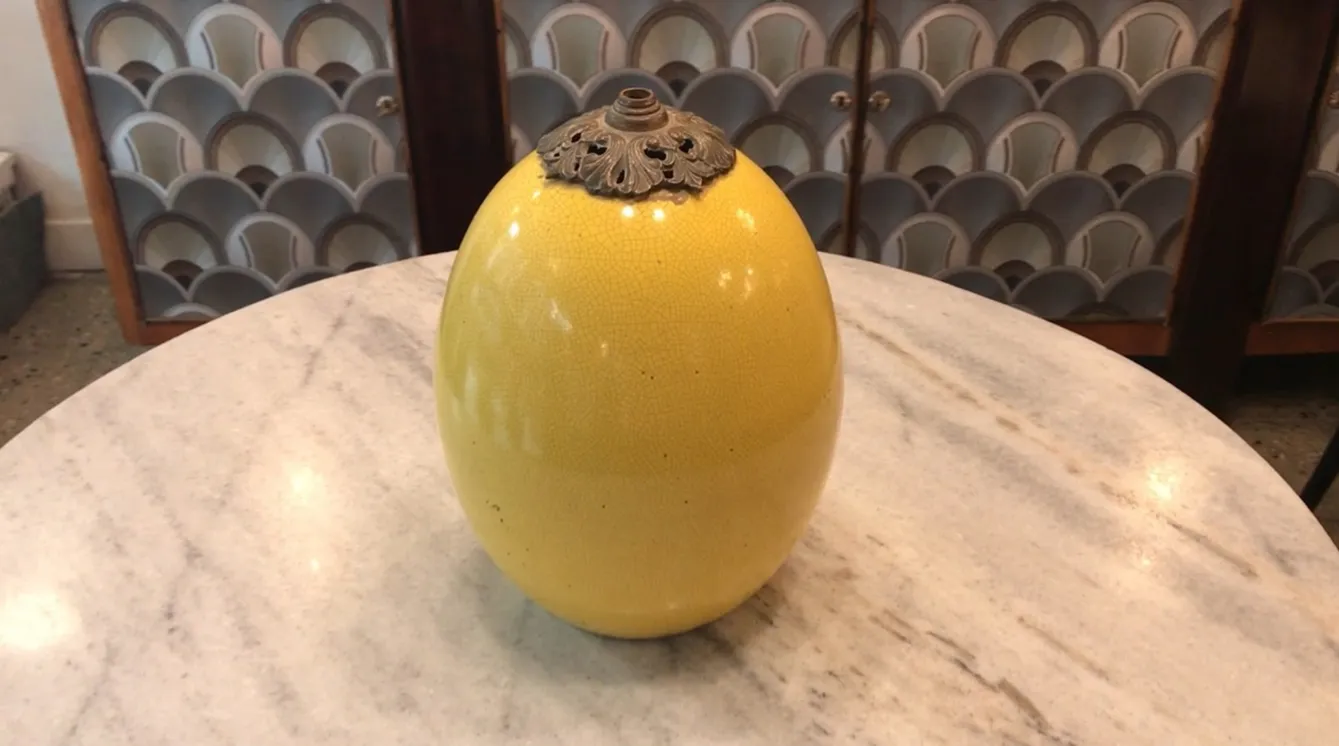 مصباح طاولة قديم من طراز آرت ديكو باللون الأصفر، ذو شكل بيضاوي وأنيق، على طاولة من الرخام.