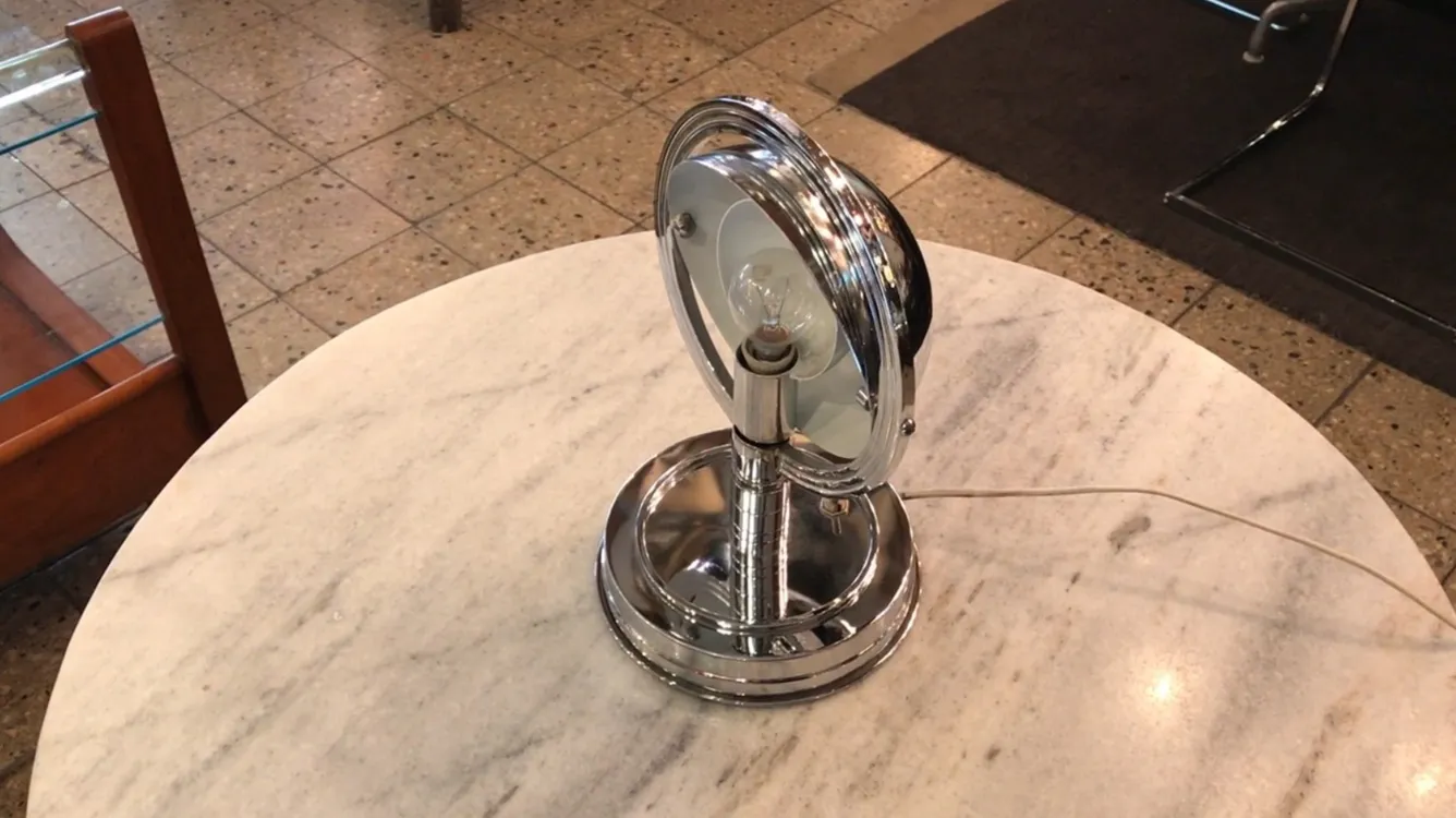 Luminária de mesa antiga com base metálica em uma mesa de mármore.