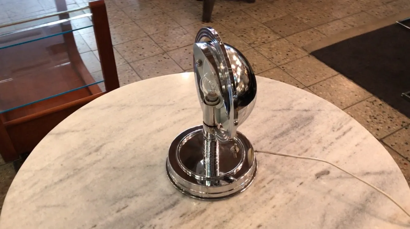 Lámpara de mesa antigua con diseño brillante en metal cromado, rodeada de un ambiente cálido.