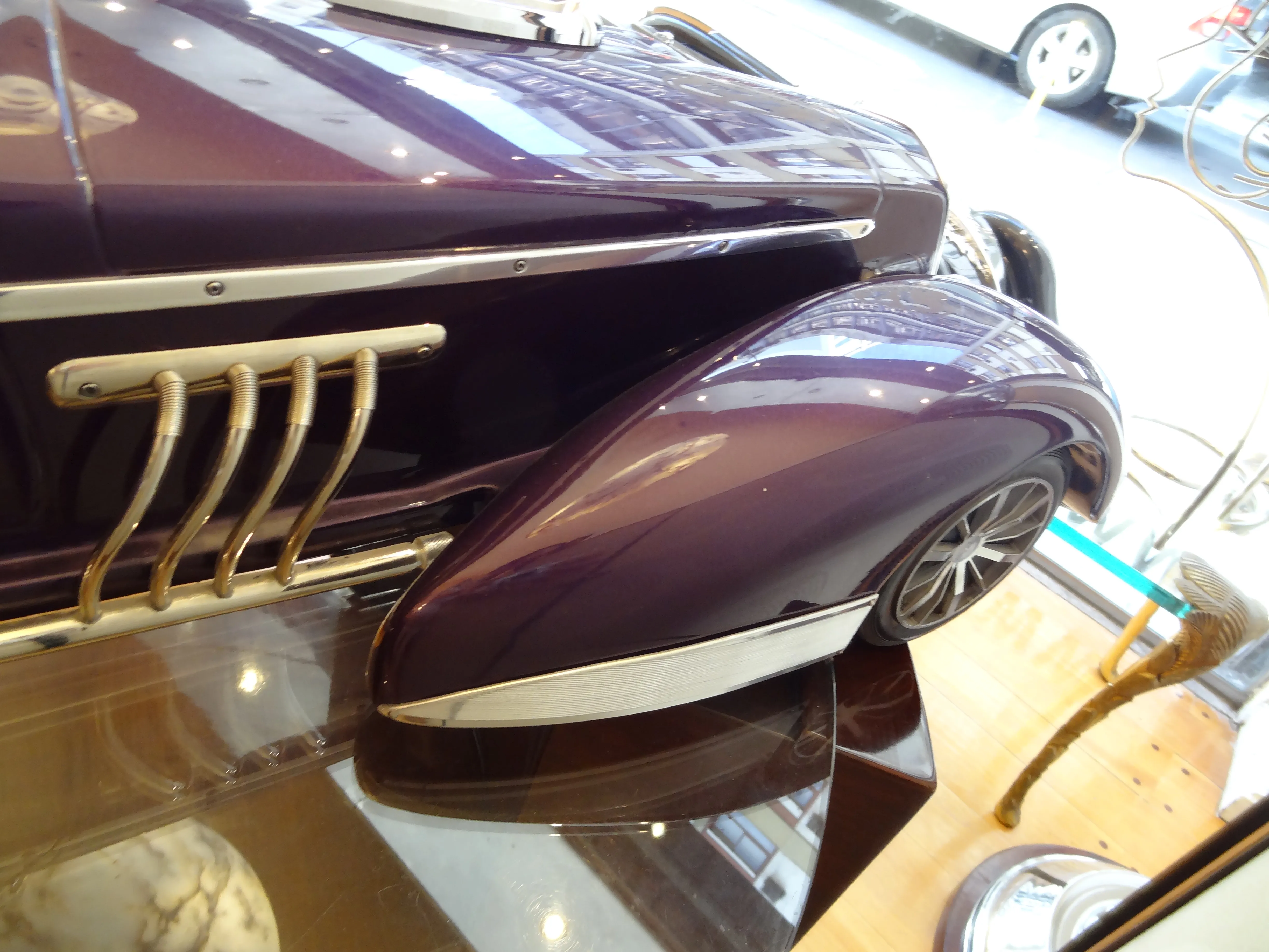 Vista lateral de um carro antigo elegante em exibição, com detalhes em dourado e cor púrpura.