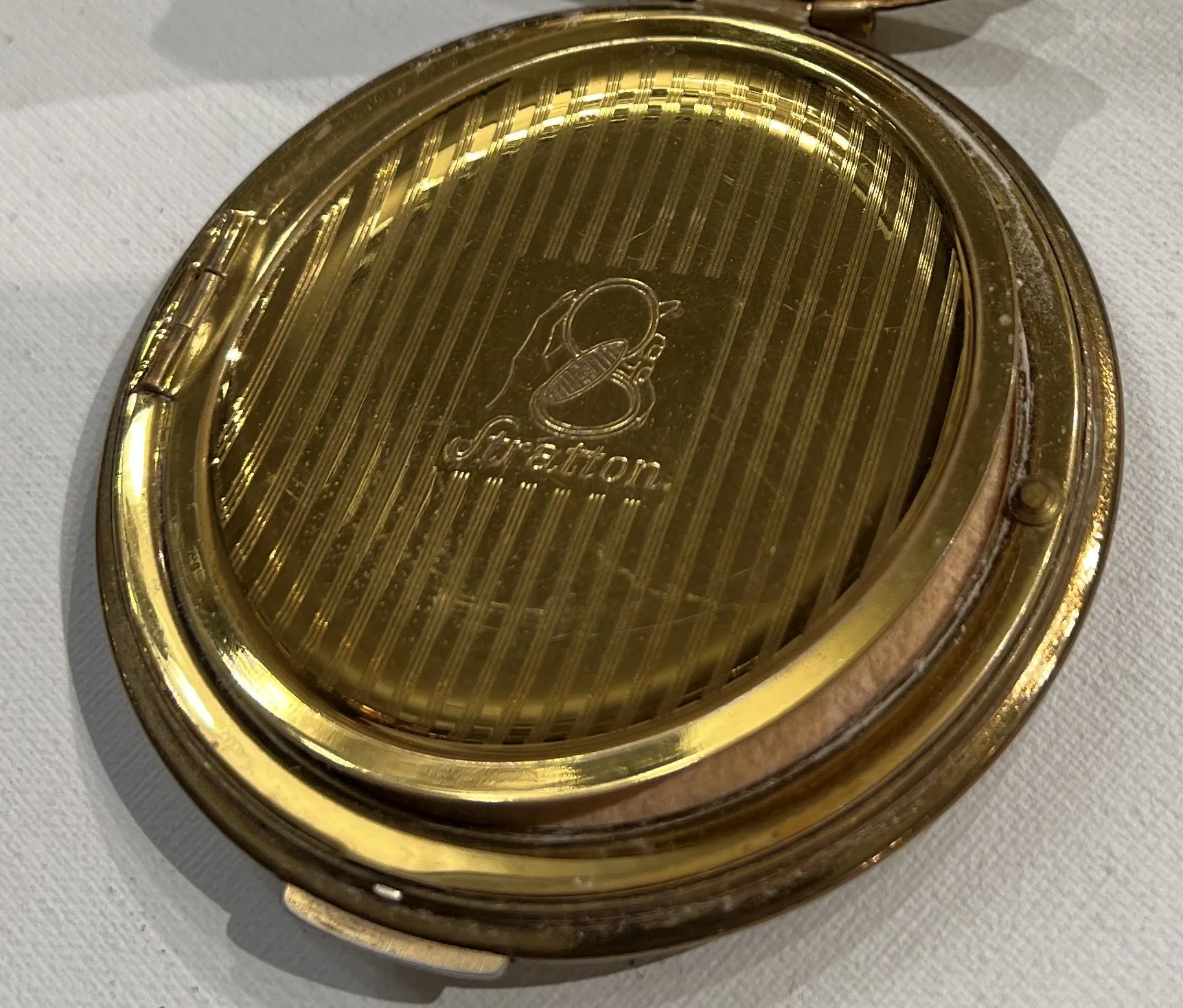 Polvera antigua con diseño elegante de Stratton England, fondo dorado.