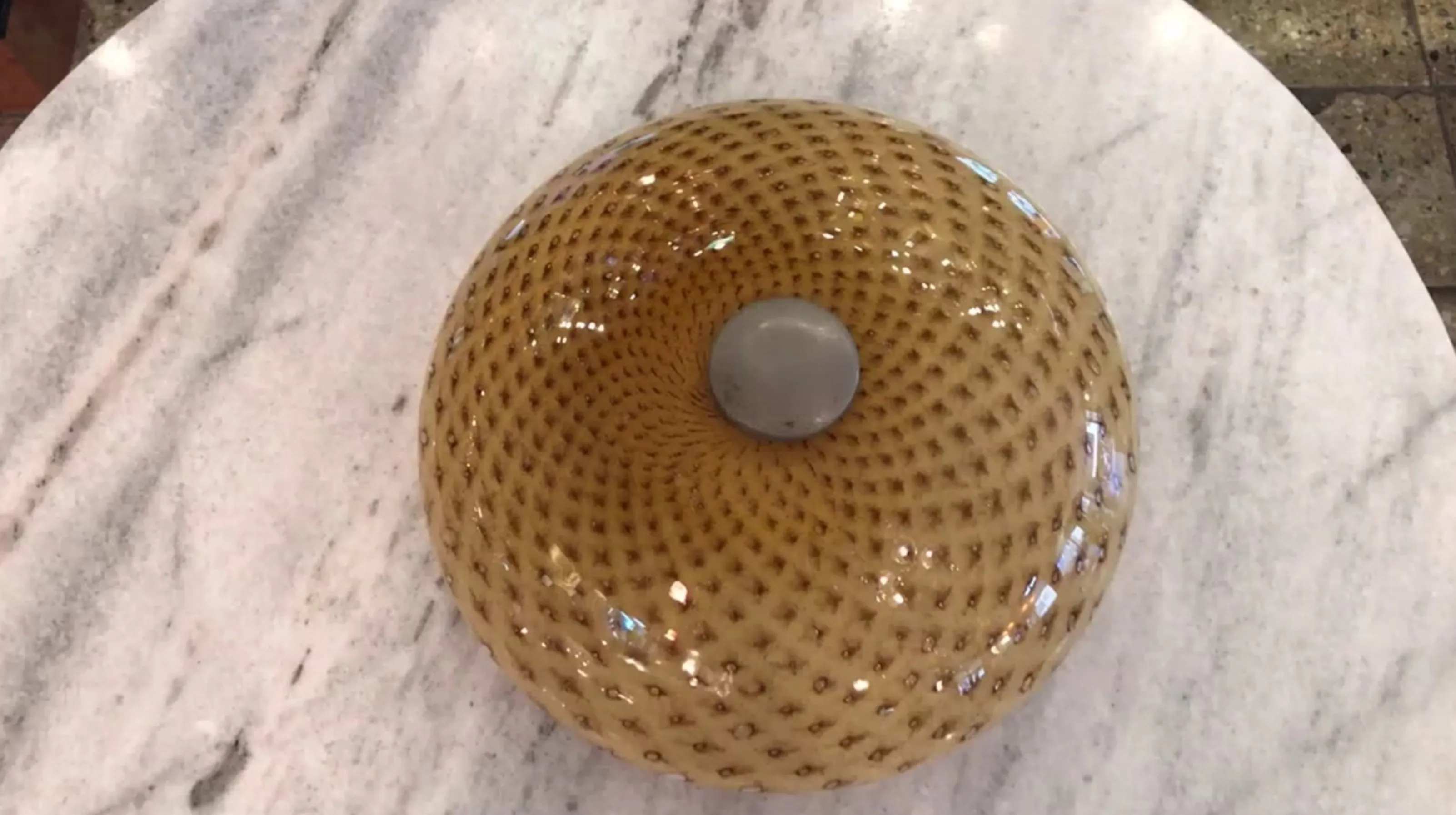 Plafón antiguo con forma esférica y diseño textual en tonos cálidos, decorando una superficie brillante.