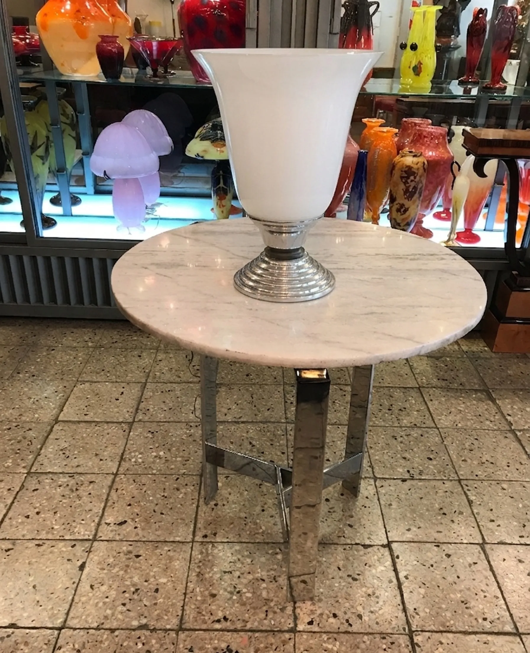 Antike Tischlampe mit glänzender Metallbasis und weißem Schirm, in einer eleganten Dekoration mit anderen dekorativen Objekten.