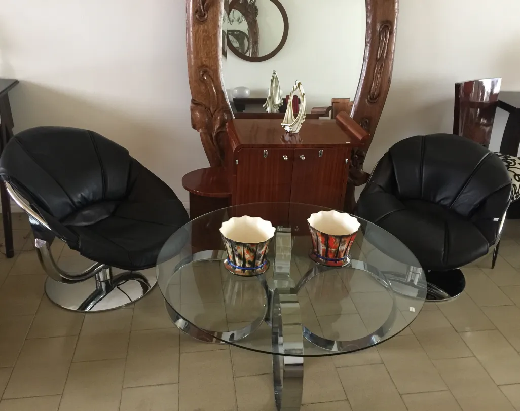 Mesa ratona antigua Art Deco con diseño elegante, acompañada de sillones negros y un entorno moderno.