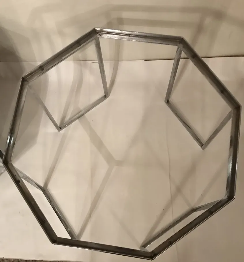 mesa de centro antiga com design octogonal e estrutura metálica, em um ambiente neutro.