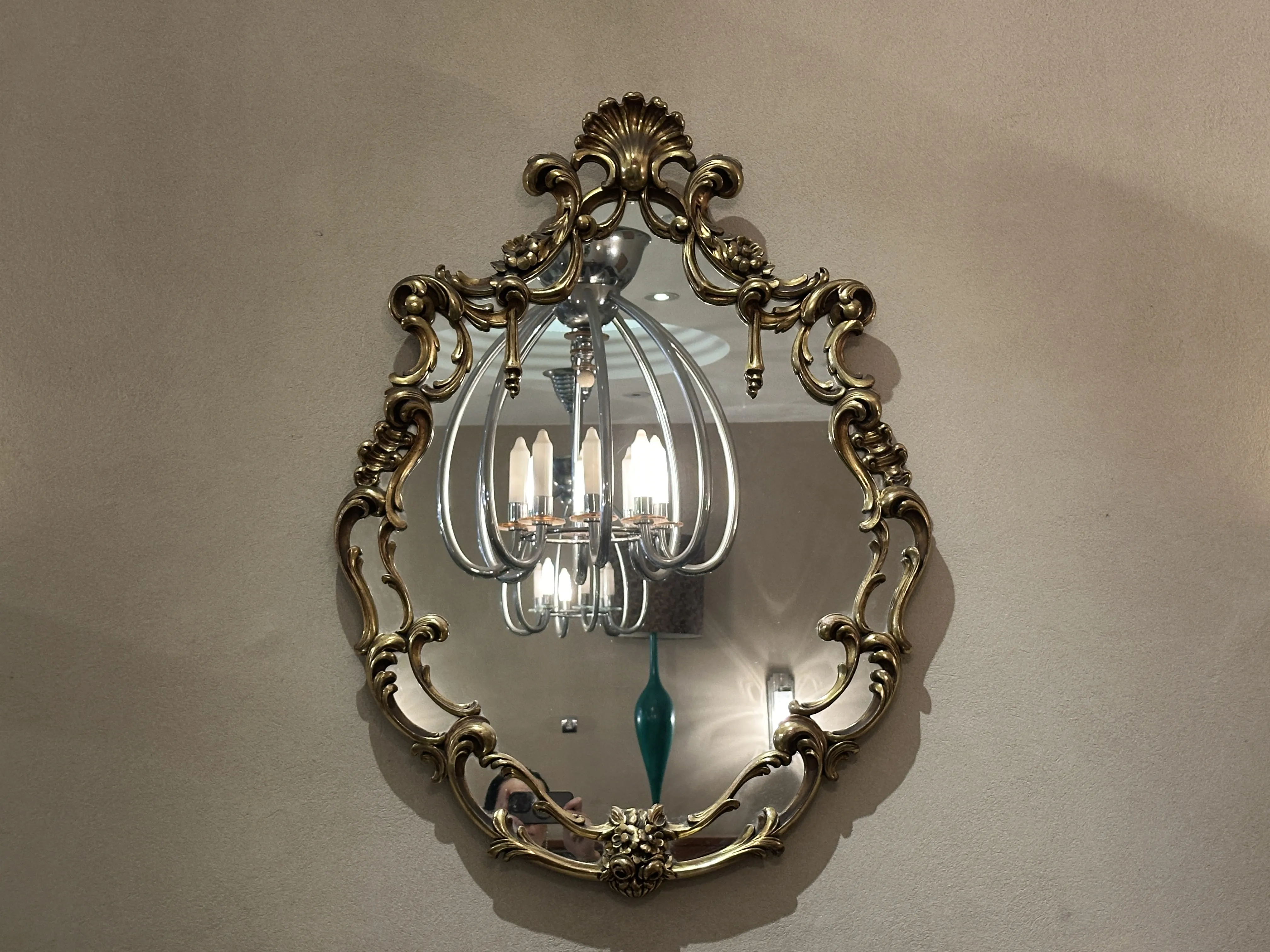 antiguo espejo decorativo de pared con marco ornamental, reflejando una lámpara y el entorno