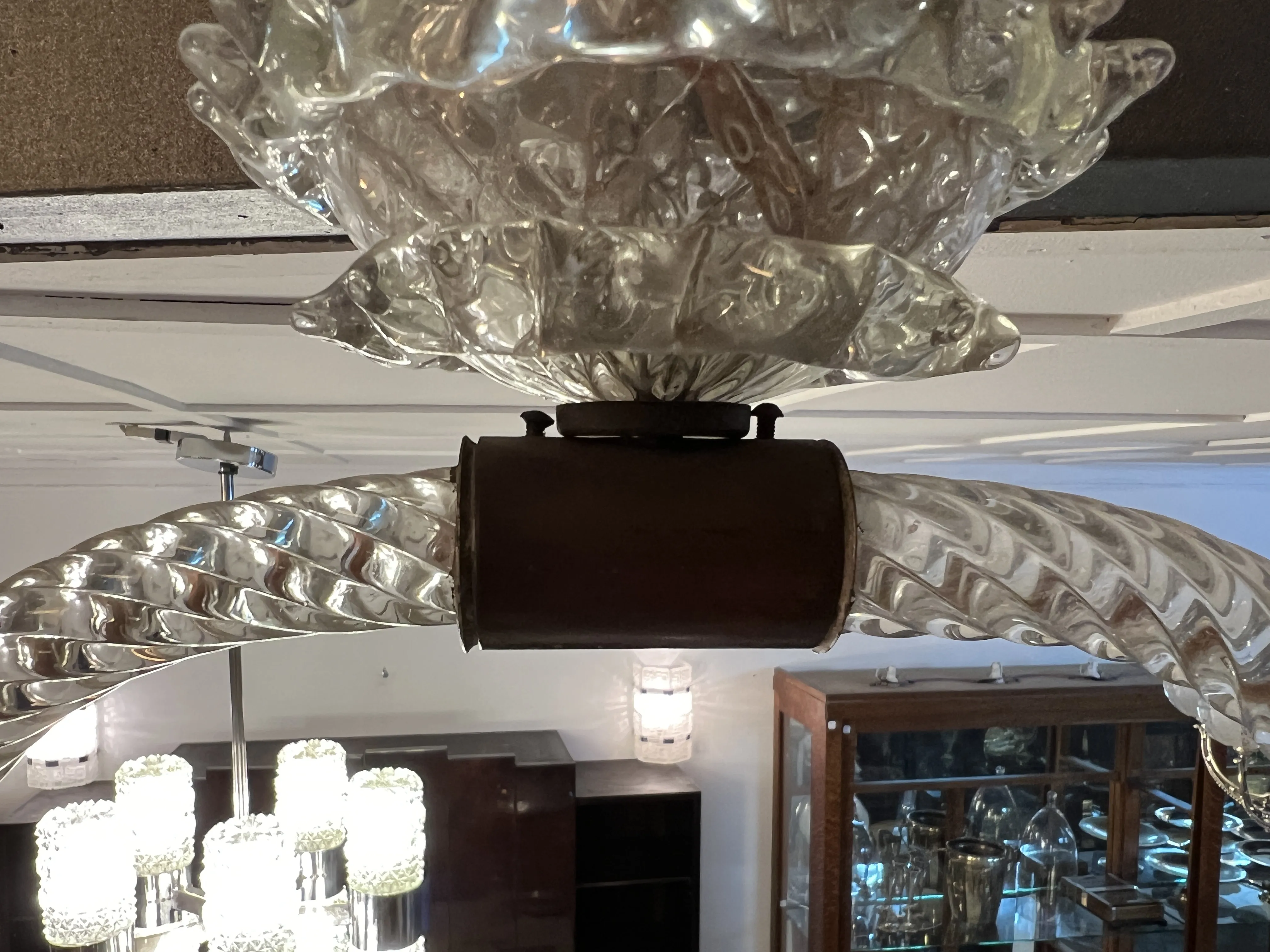 Vue d'un ancien lustre Mazzega Murano avec des détails en verre, lumières allumées à l'arrière-plan.