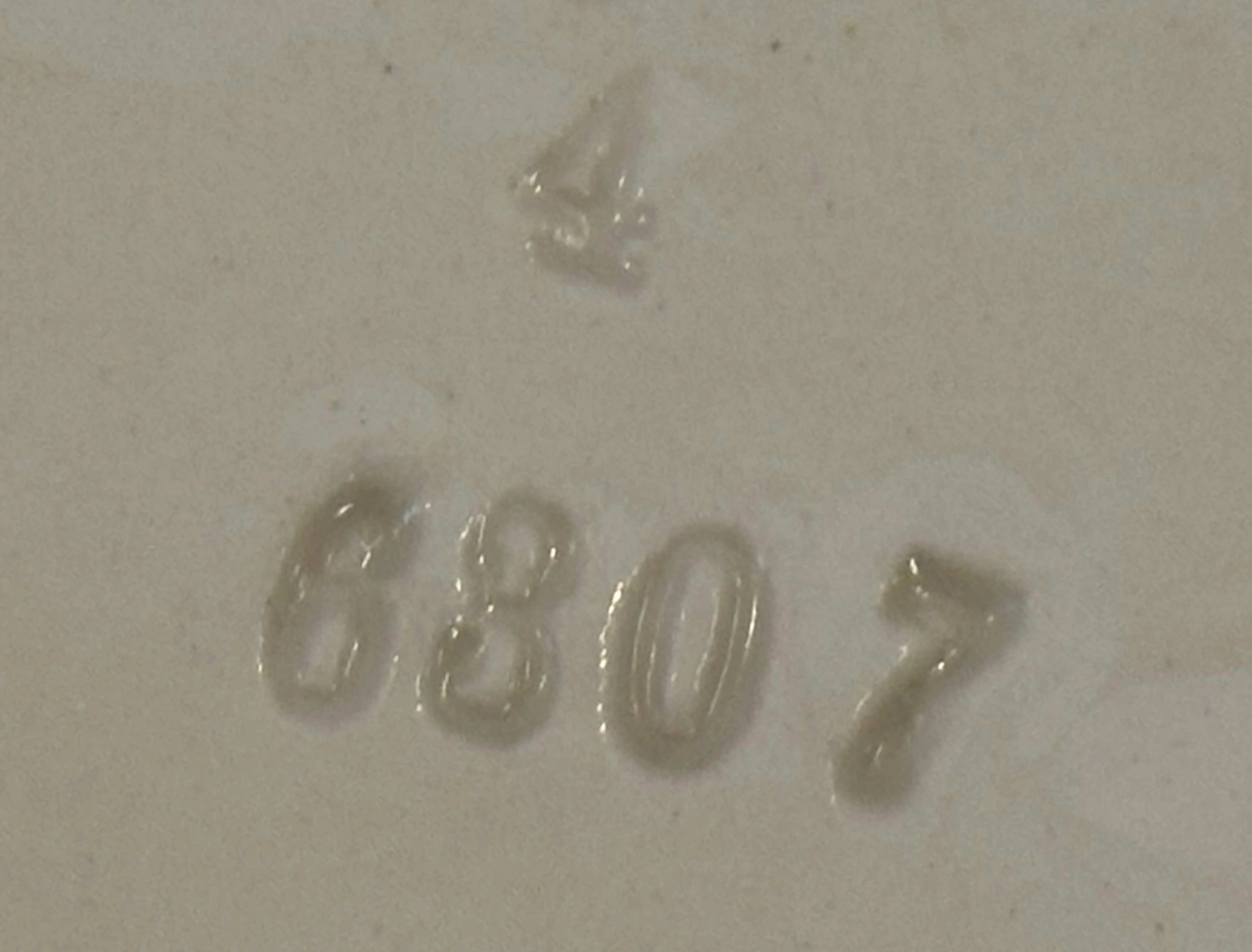 Cerámica antigua con numeración en relieve sobre fondo claro.
