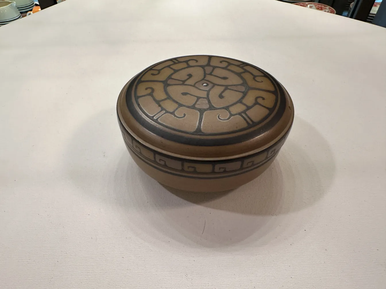 Antigua cerámica con diseño en la tapa y un patrón