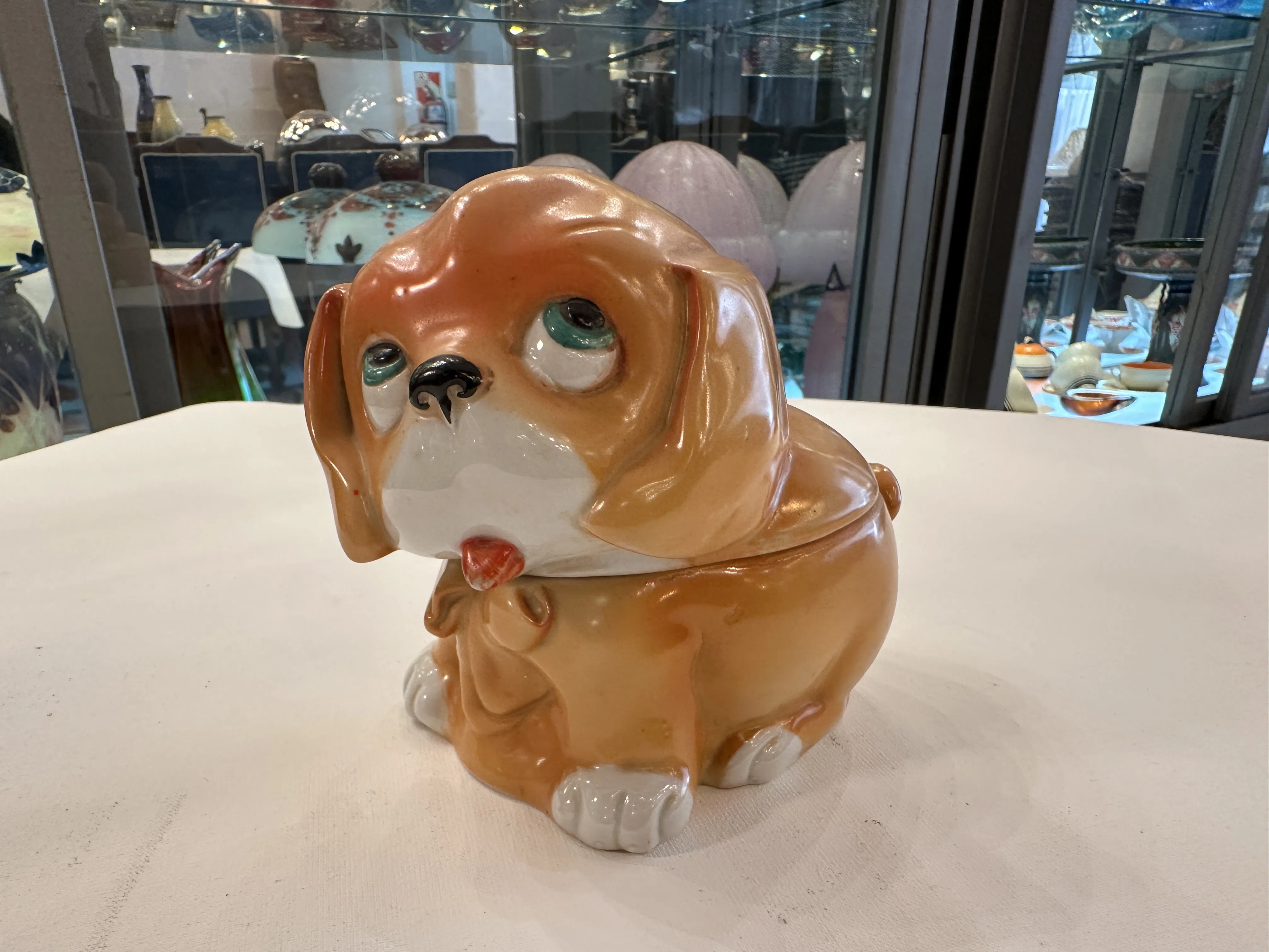 figurinha de cachorro de cerâmica antiga com detalhes coloridos, olhos grandes e expressão doce, ambientada em uma loja de antiguidades.
