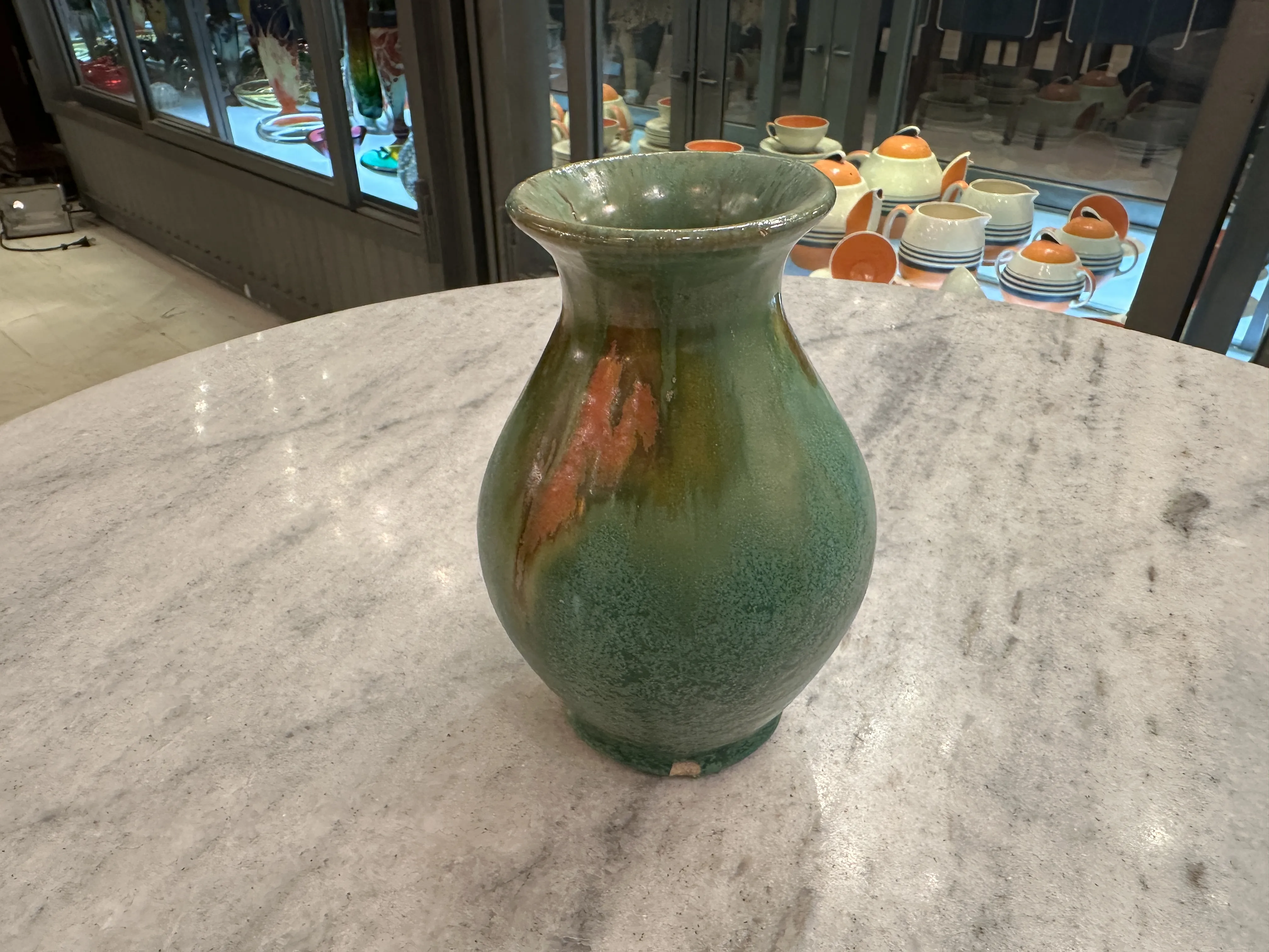 Jarrón antiguo de cerámica verde decorativa en una mesa de mármol.