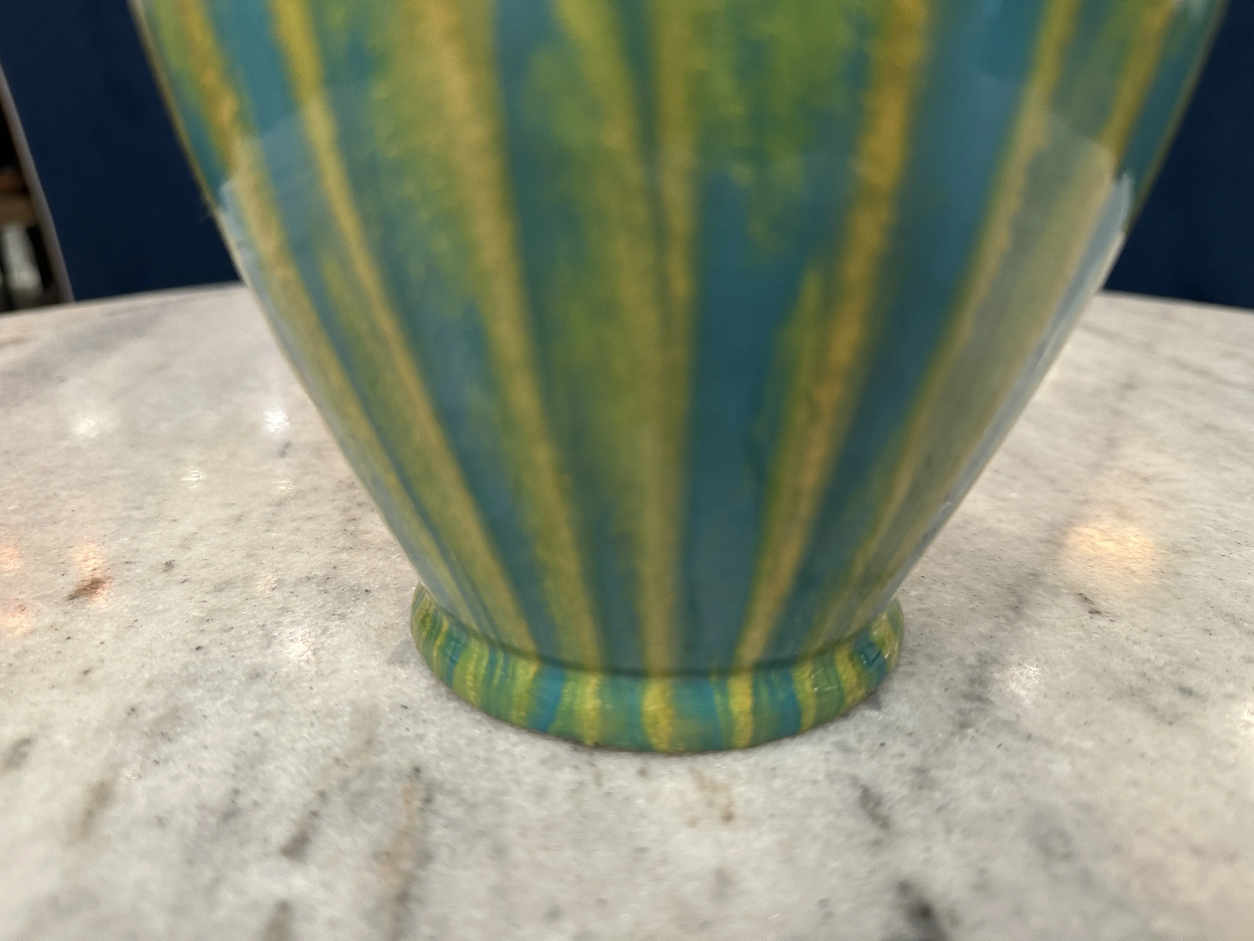 Ancienne céramique colorée avec un motif vert et jaune sur une base sur une table.