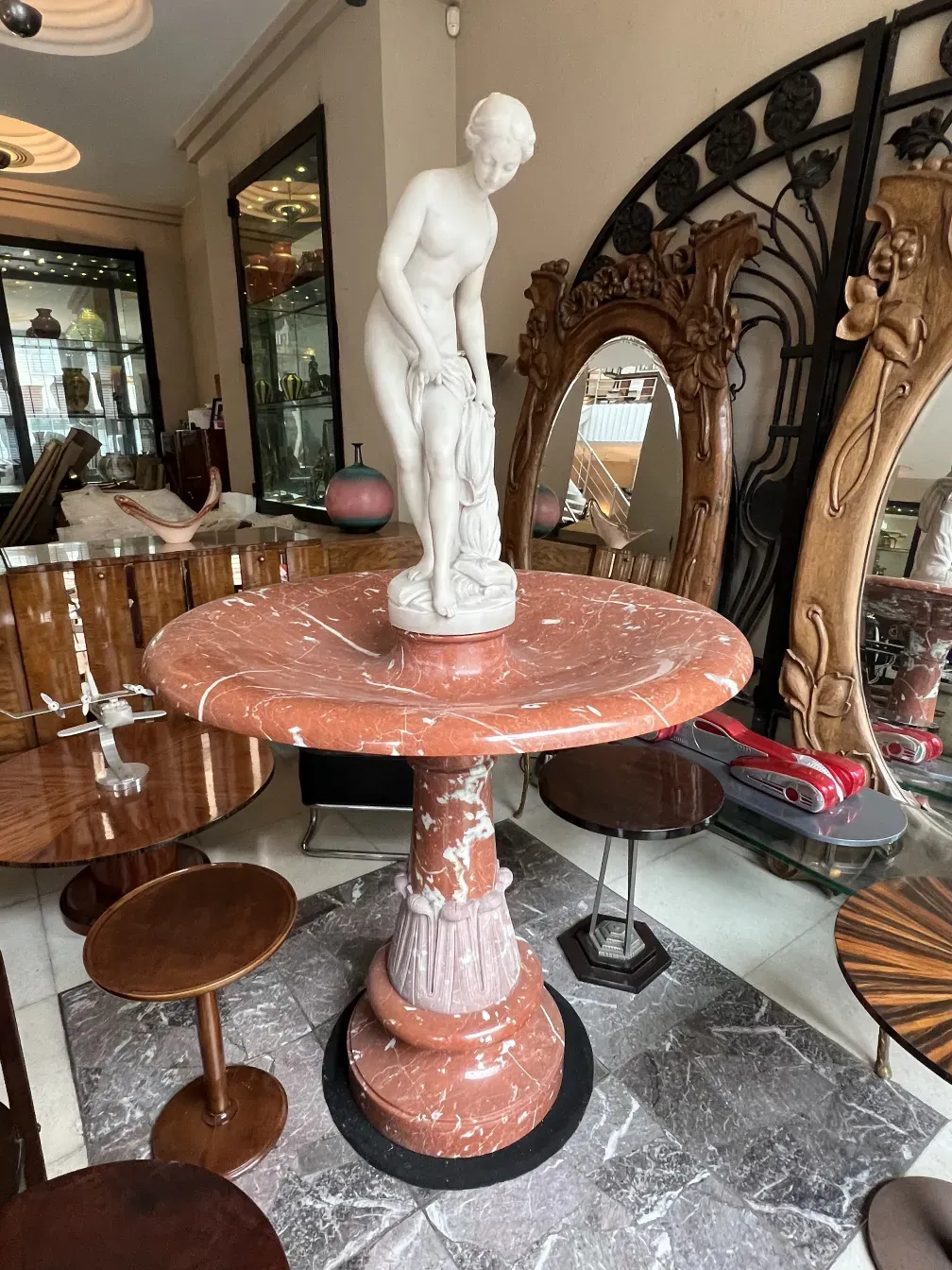 Fontana antica in stile art nouveau con scultura centrale, circondata da oggetti decorativi.