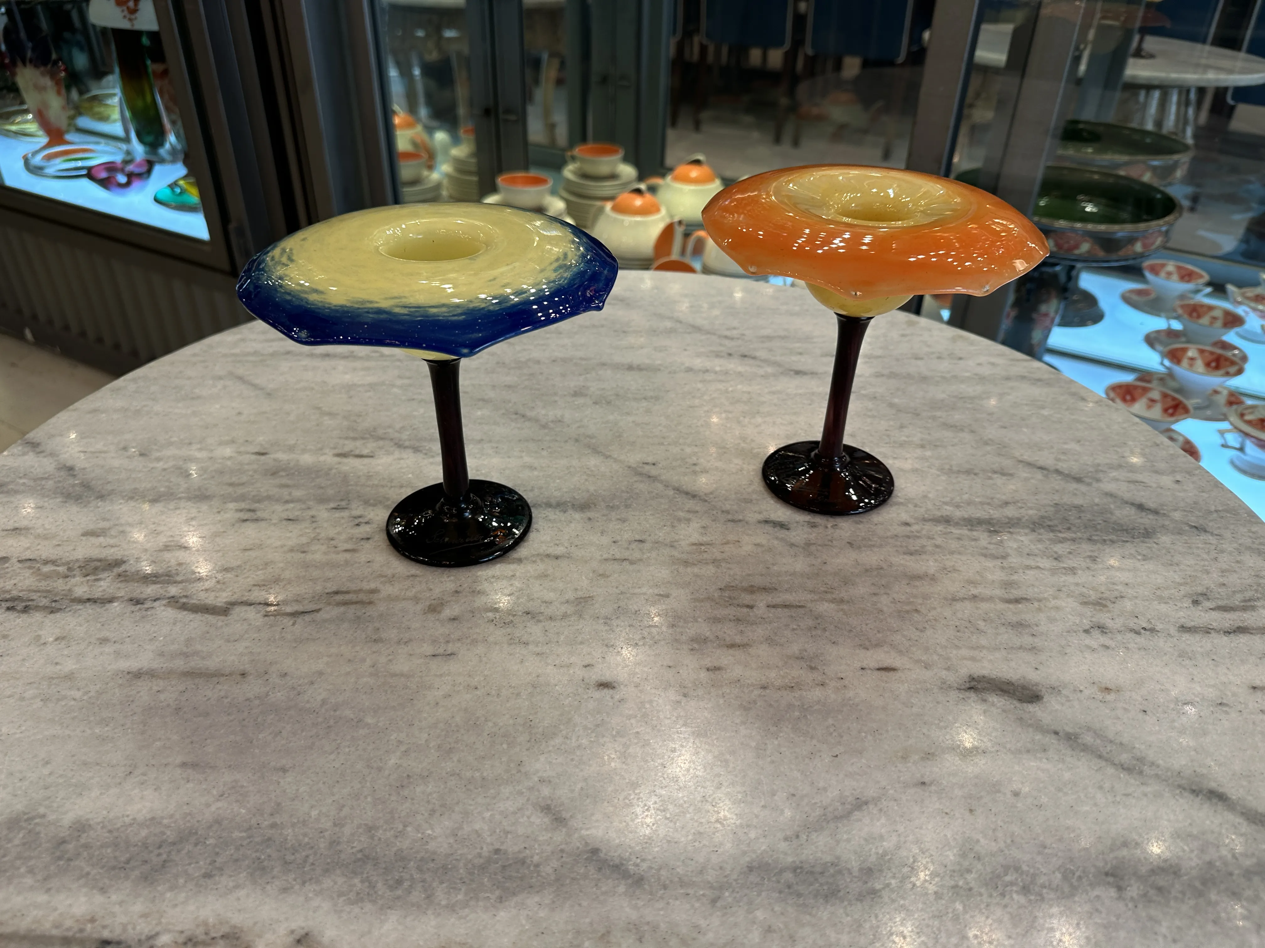 シュナイダーのサイン入りの古い杯が2つあります。1つは青、もう1つはオレンジで、大理石のテーブルの上にあります。