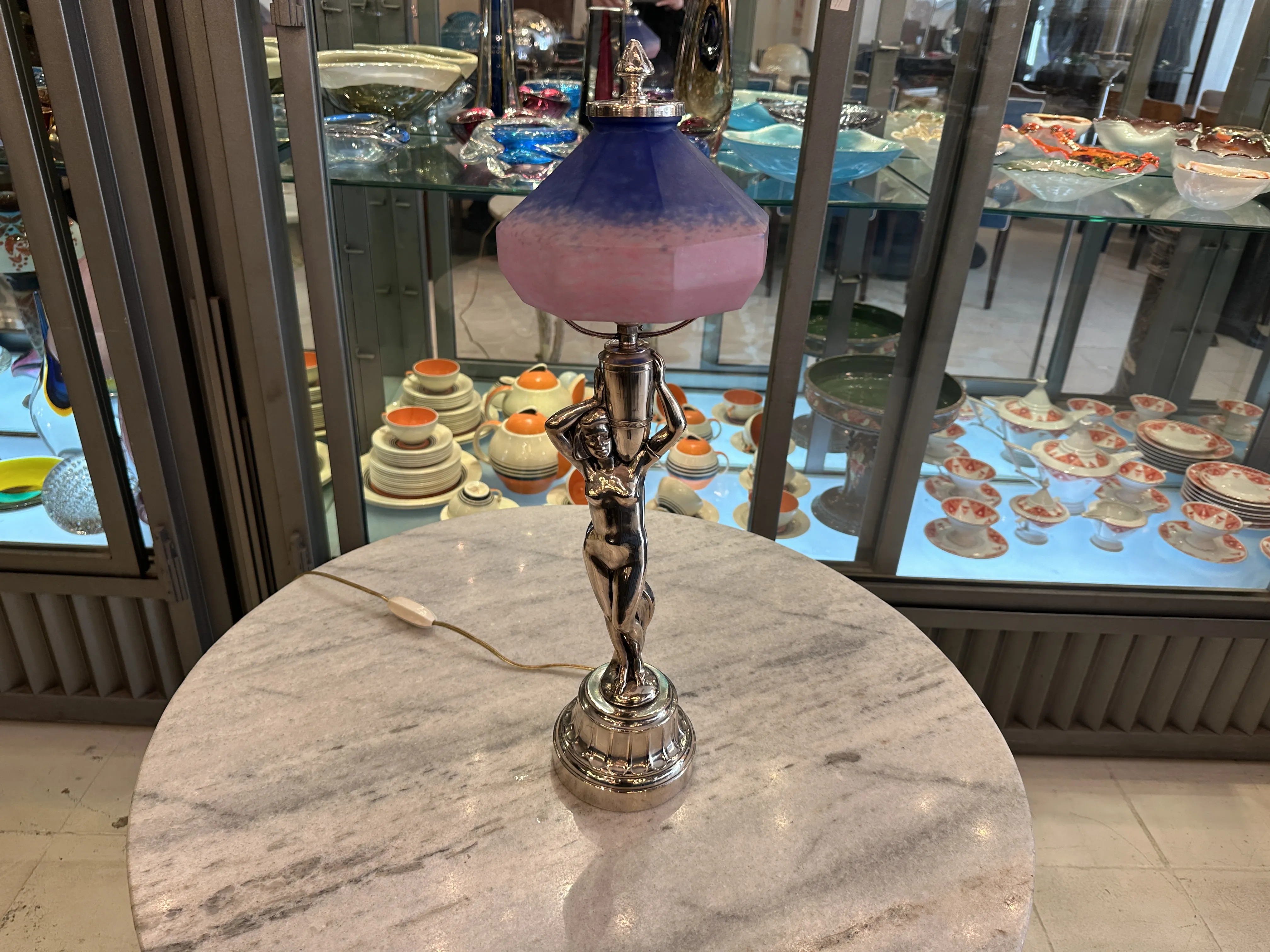 Antique table lamp featuring a shiny base and a colorful shade, set in an elegant environment with decorative objects.