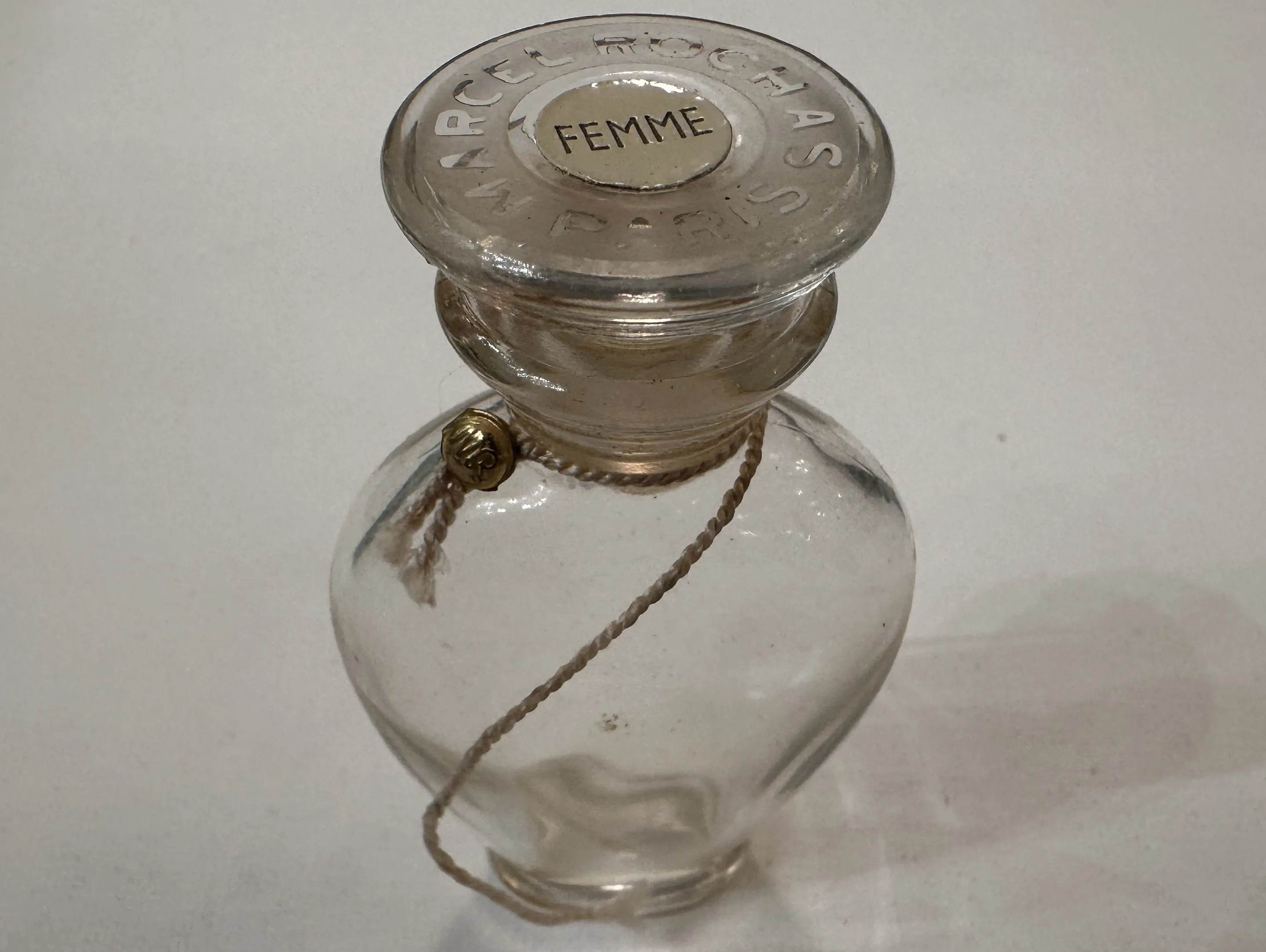 Frasco antiguo de perfume con tapa decorativa y cuerda.